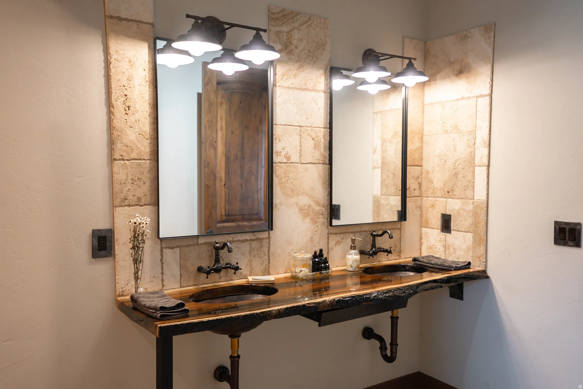 Dual vanity featuring a live-edge wood countertop with integrated sinks, wall-mounted bronze-finish faucets, and industrial-style exposed plumbing