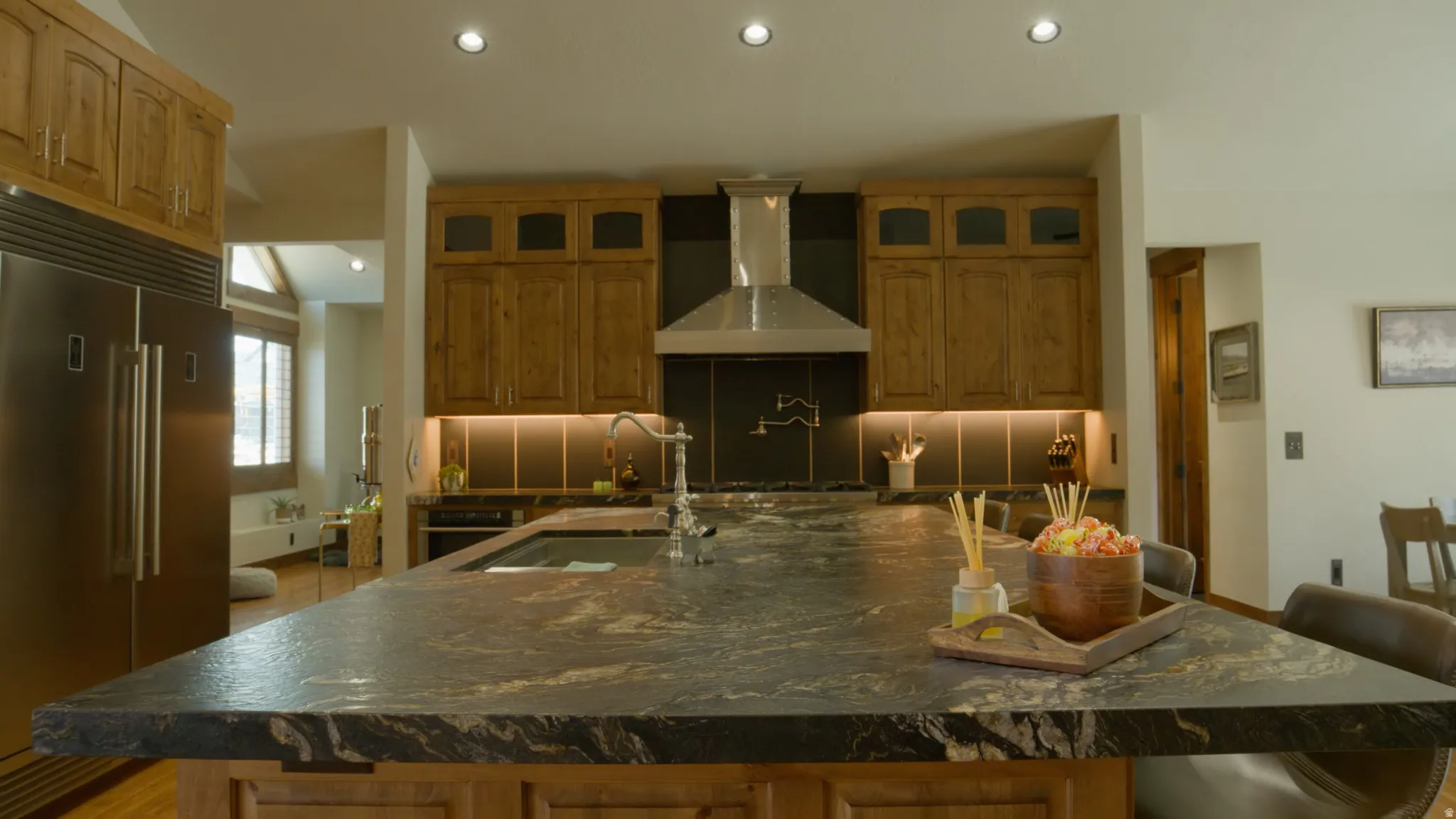 Kitchen featuring a large central island with a built-in sink, natural wood cabinetry, stainless steel appliances, under-cabinet lighting, and recessed ceiling lights