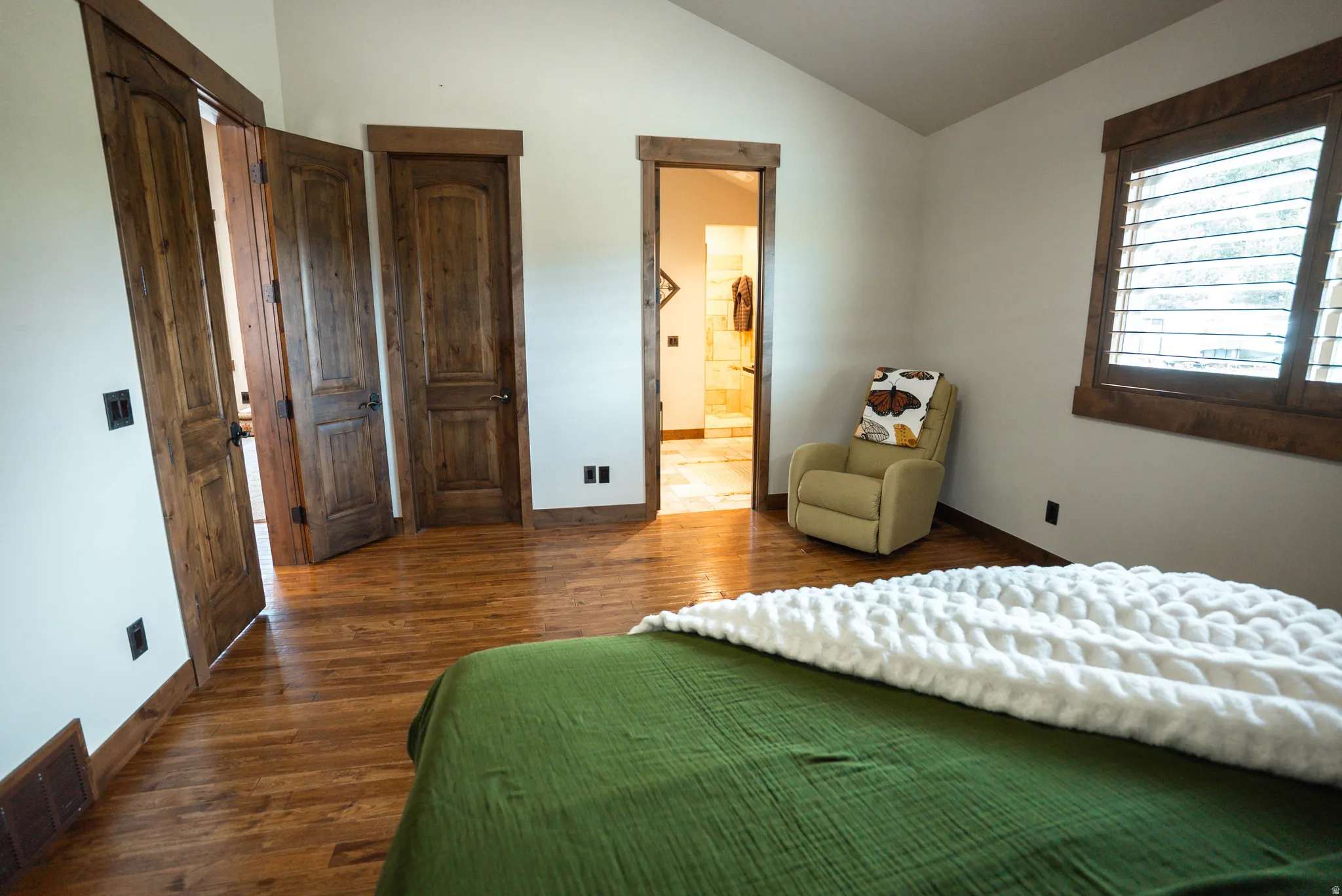Spacious room featuring wood-finish flooring, vaulted ceilings, and a window with plantation shutters