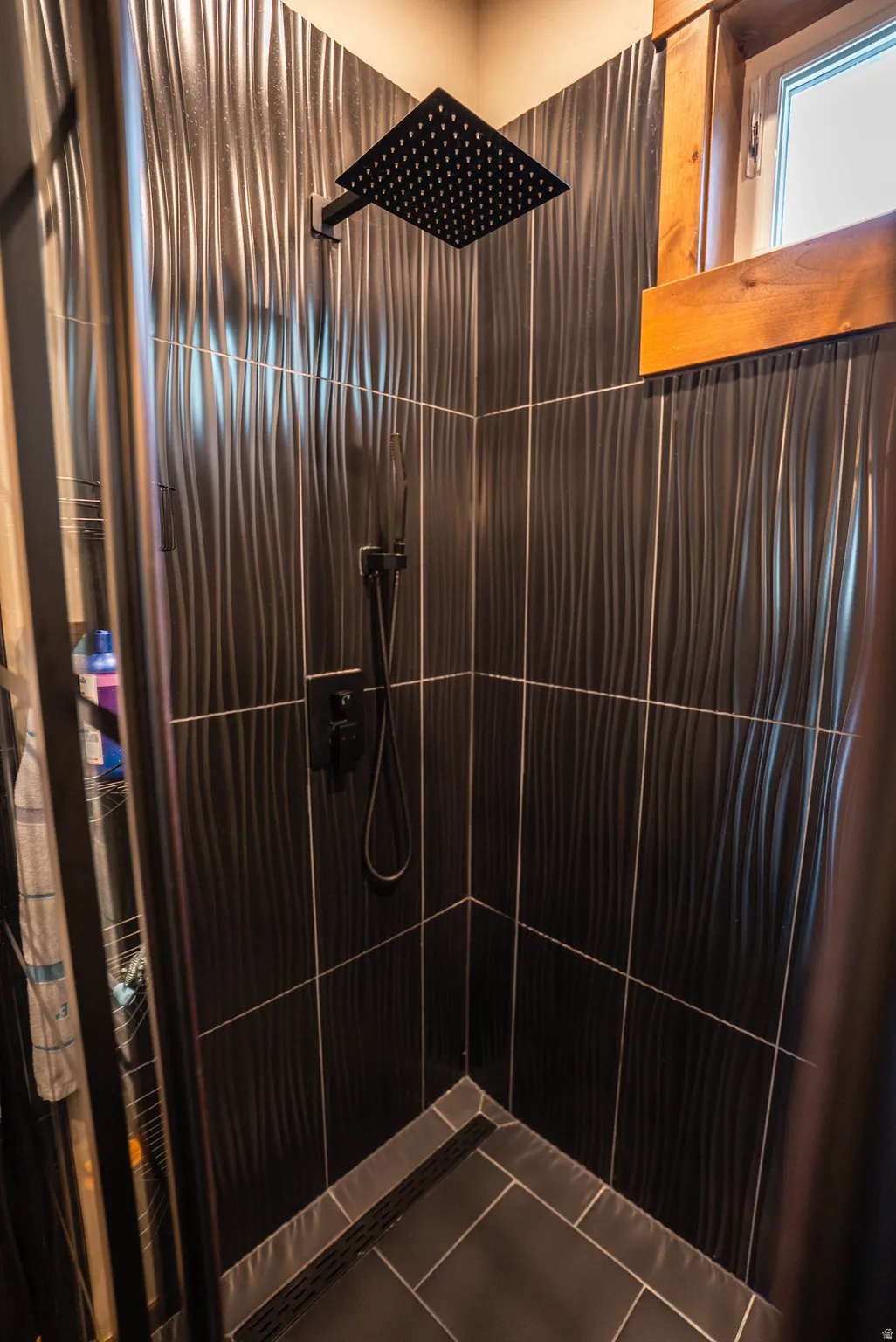 Shower stall featuring dark, textured wall tiles and a matte black rain shower head