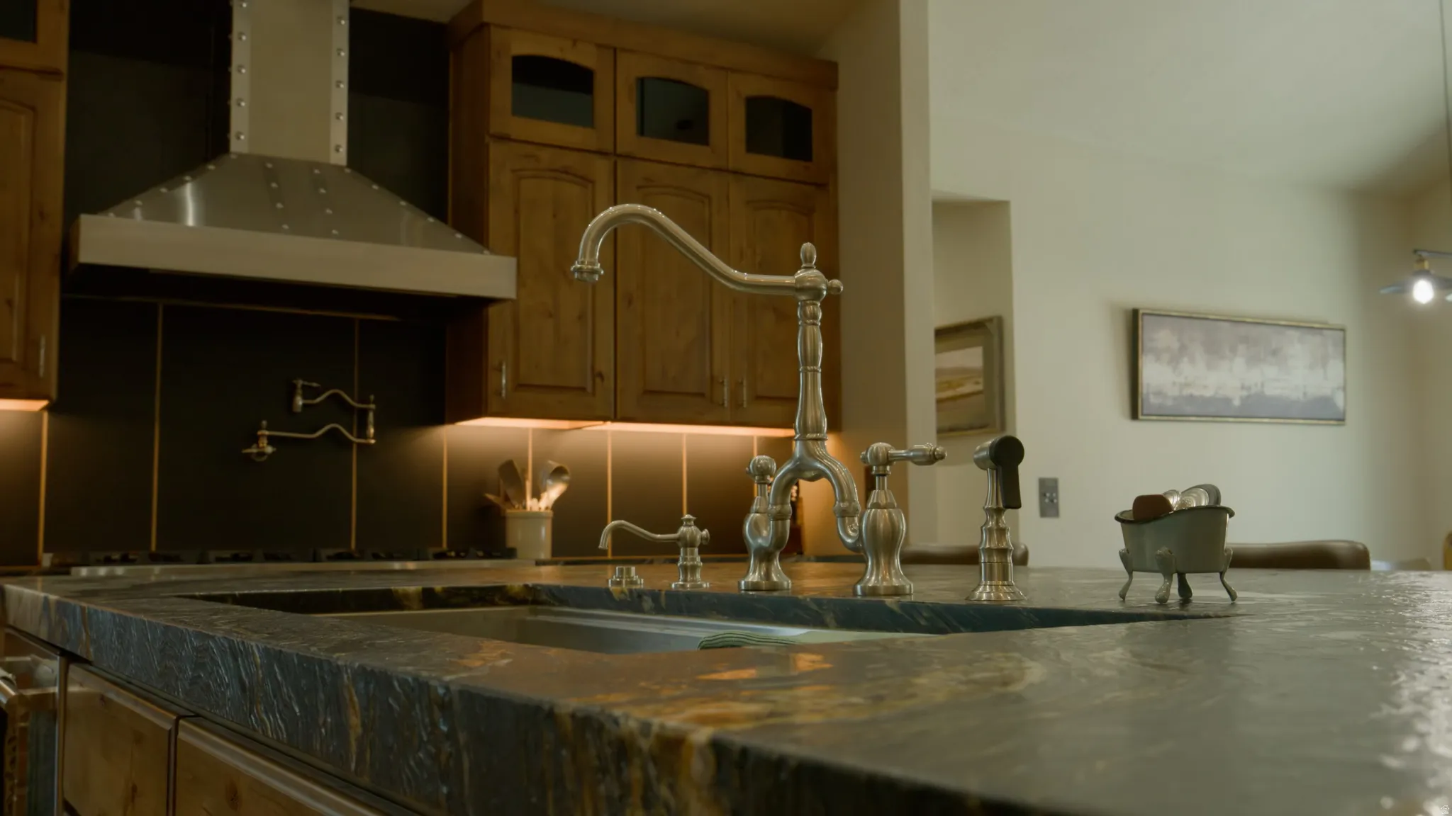 Kitchen featuring a large stainless steel range hood, wooden cabinetry with glass inserts, a dark backsplash, under-cabinet lighting, and a multi-toned stone countertop with an integrated sink and brushed nickel faucet