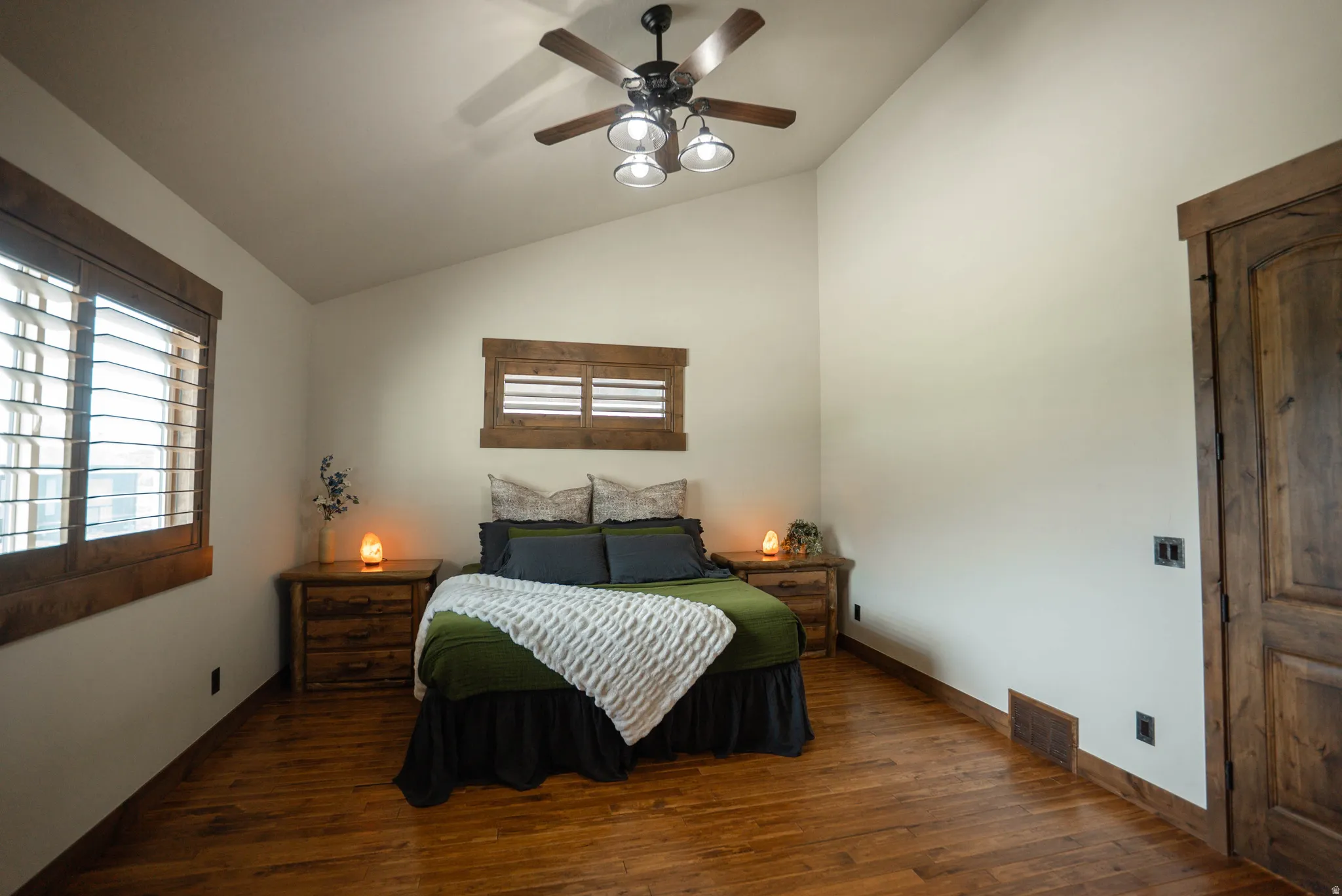 Vaulted ceiling bedroom featuring wood-finish flooring, plantation shutters, and a ceiling fan with integrated lighting