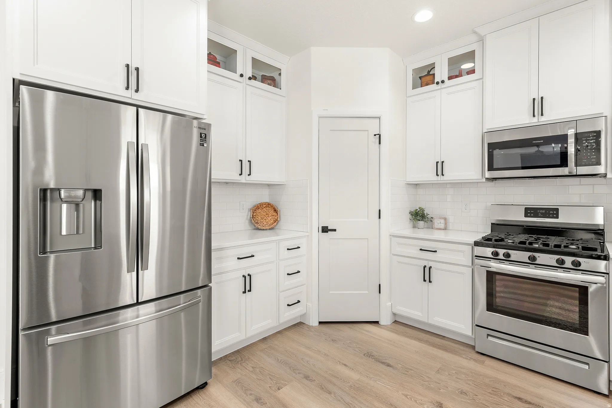 Kitchen featuring white cabinetry with dark hardware, stainless steel appliances including a French door refrigerator and gas range, white subway tile backsplash, light wood-finish flooring, and white countertops