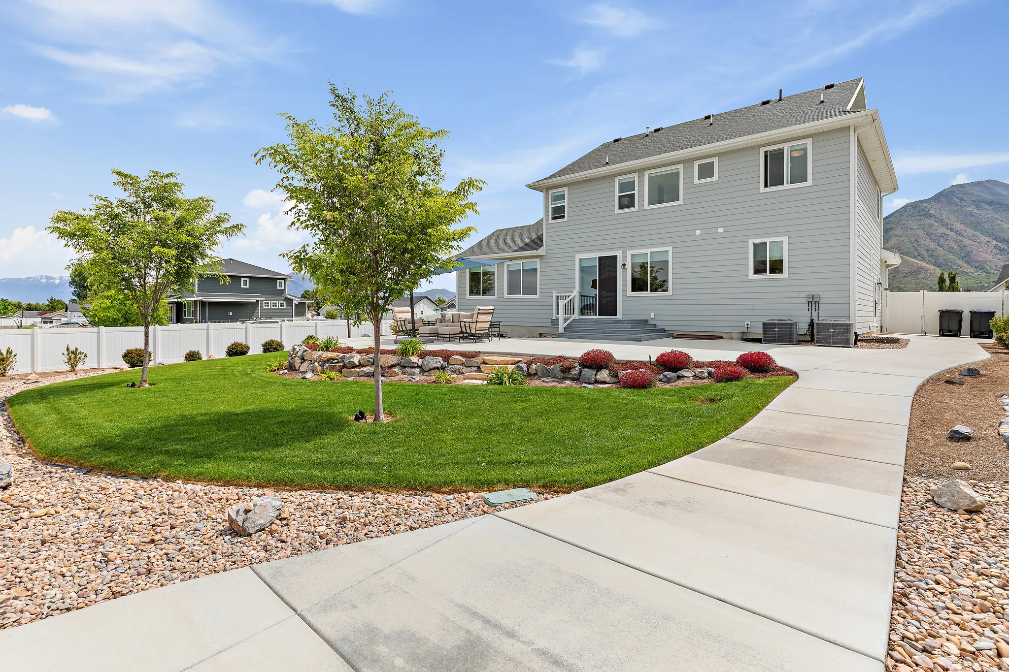 Expansive backyard featuring a manicured lawn, concrete patio, and mature trees