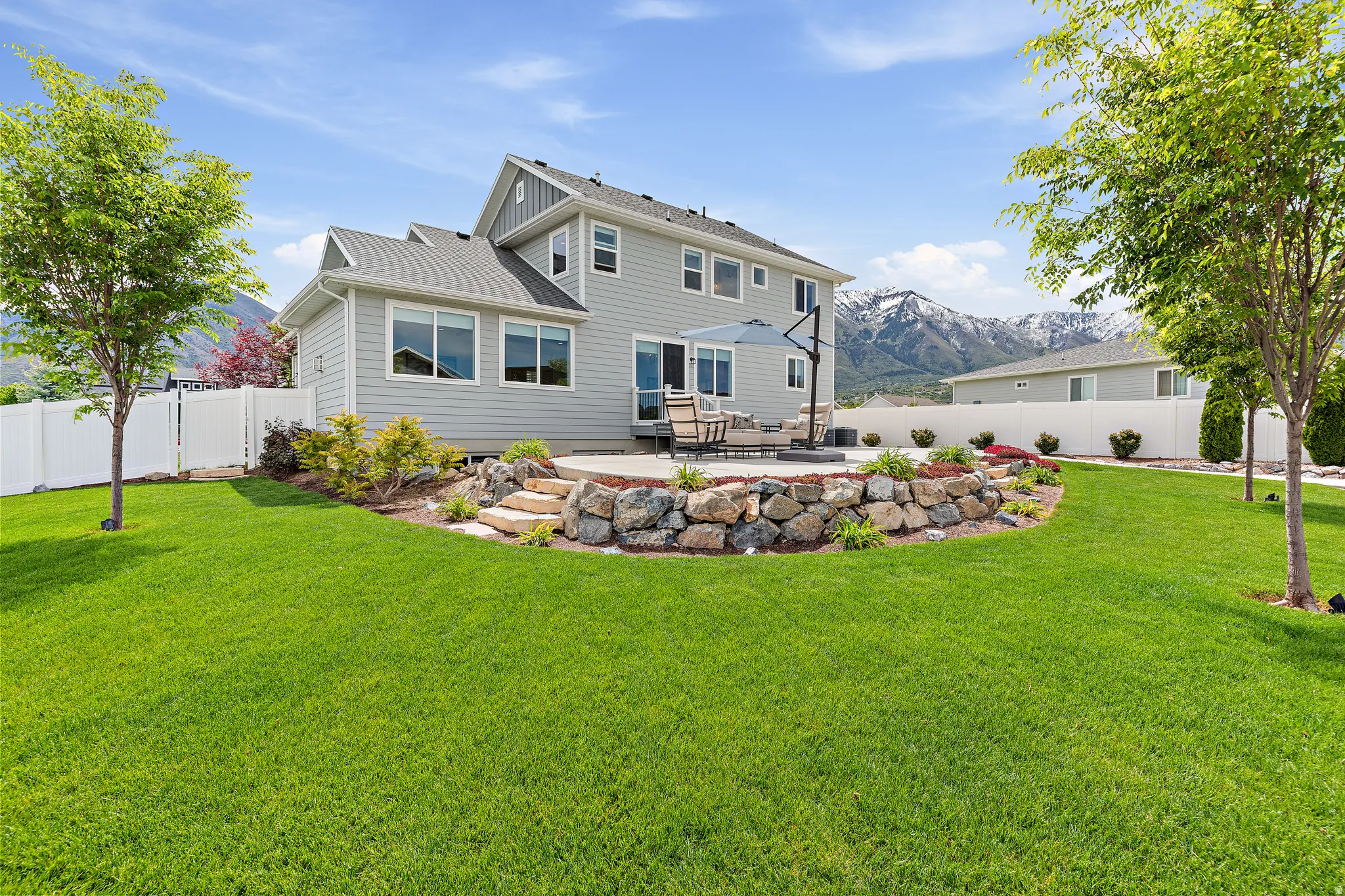 Spacious backyard featuring a large green lawn, a stone-tiered patio, and a retaining wall with integrated landscaping