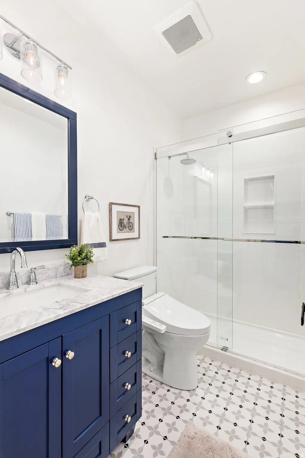 Bathroom with a navy blue vanity featuring a stone countertop and an undermount sink, a glass-enclosed shower with a built-in niche, and patterned floor tiling