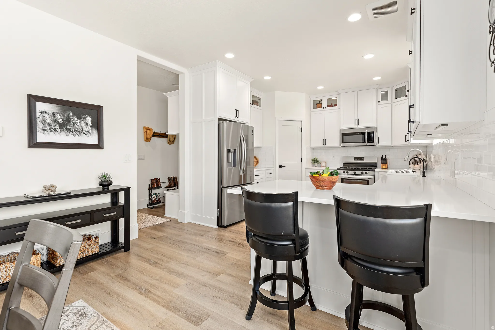 Contemporary kitchen featuring white cabinetry, stainless steel appliances, a white subway tile backsplash, and light wood-finish flooring