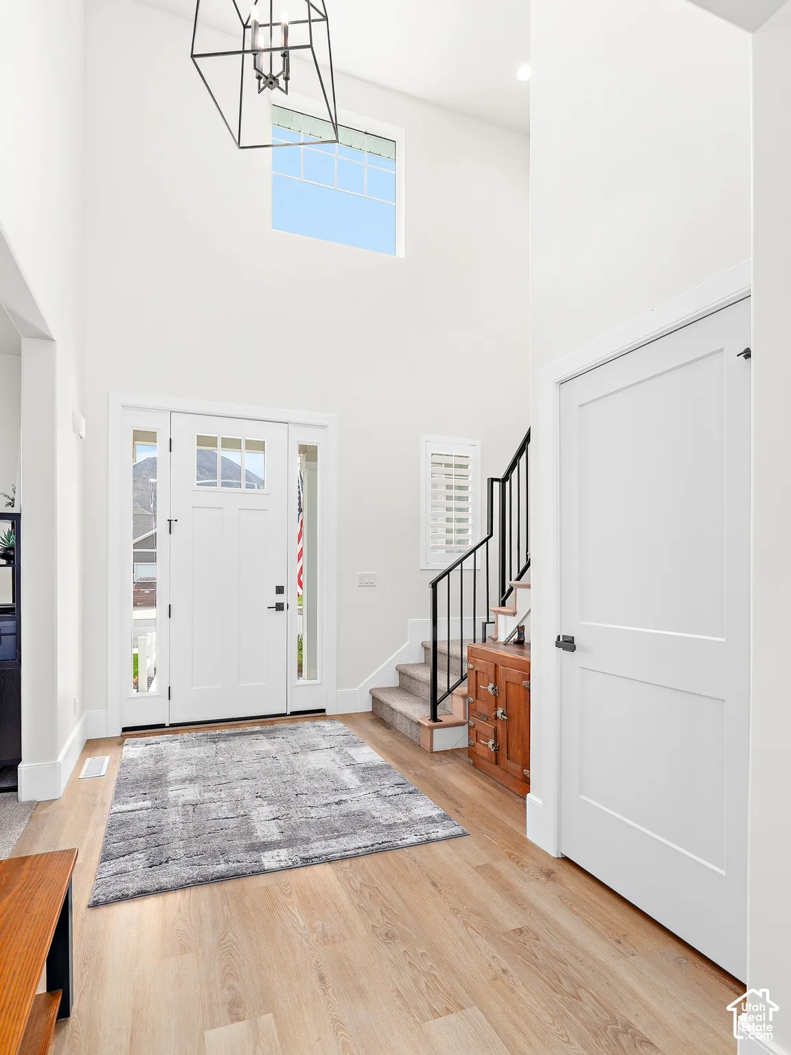 Two-story foyer featuring light wood-finish flooring, a contemporary chandelier, and a prominent transom window