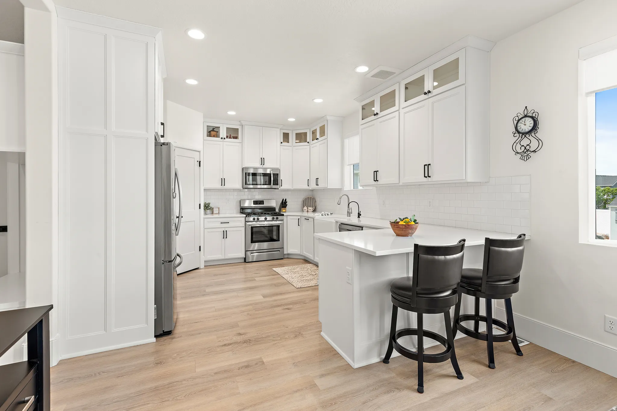 Bright kitchen featuring white cabinetry, stainless steel appliances, a white subway tile backsplash, light wood-finish flooring, and a peninsula with countertop seating