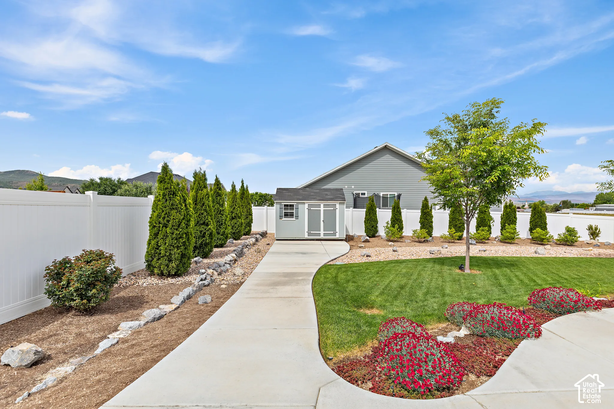 Expansive backyard featuring a lush lawn, mature landscaping, and a white privacy fence