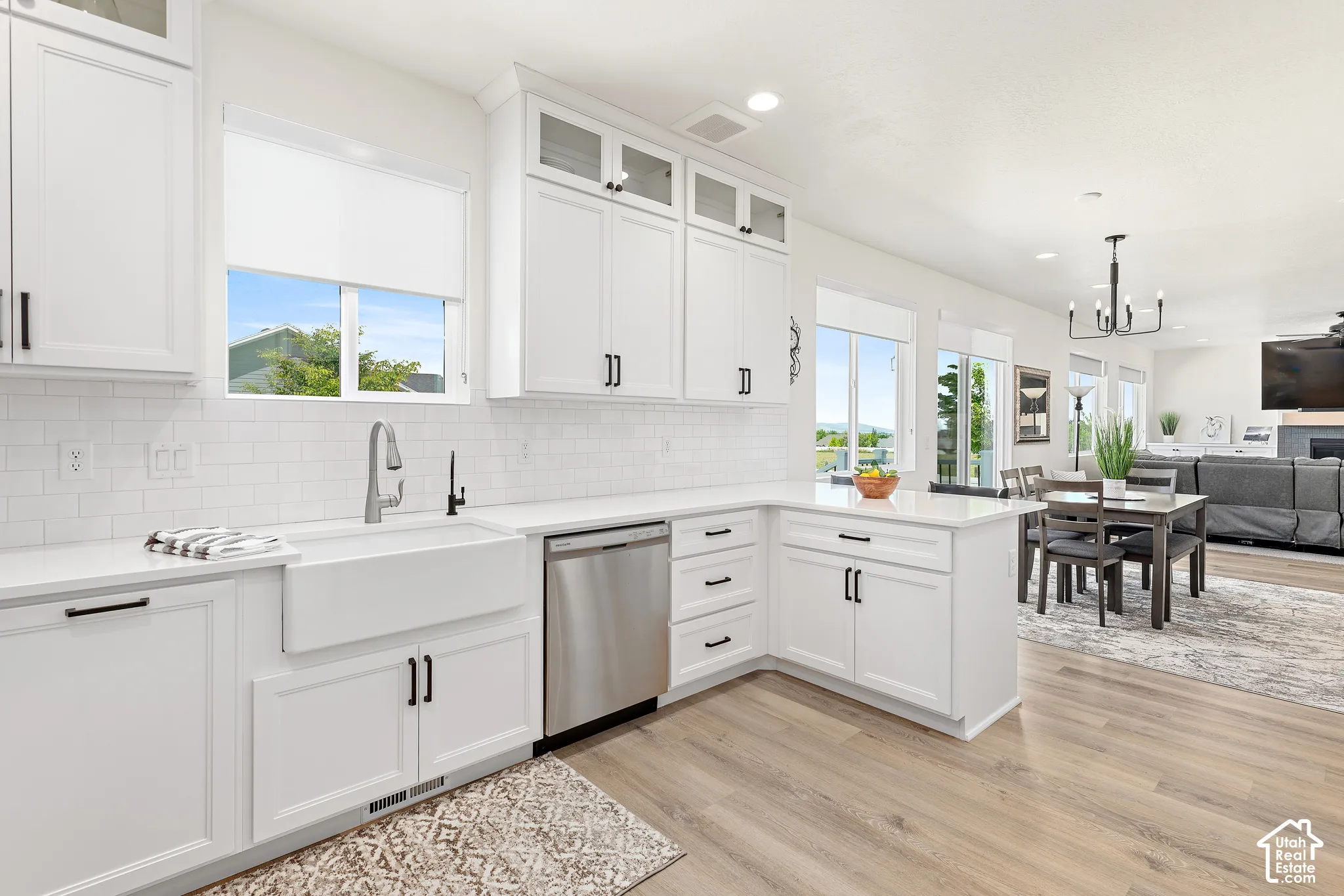 Bright kitchen featuring white shaker cabinetry, an apron front sink, stainless steel dishwasher, and wood-finish flooring