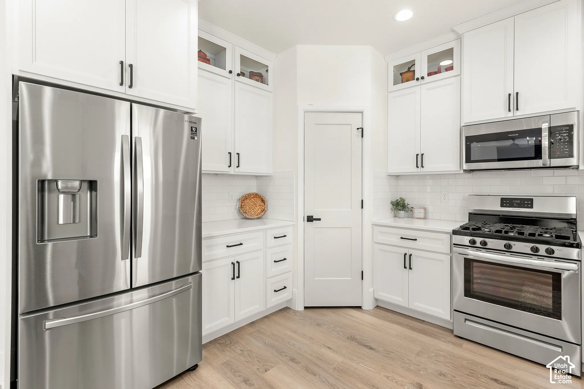Kitchen featuring white cabinetry with dark hardware, stainless steel appliances including a French door refrigerator and gas range, white subway tile backsplash, light wood-finish flooring, and white countertops