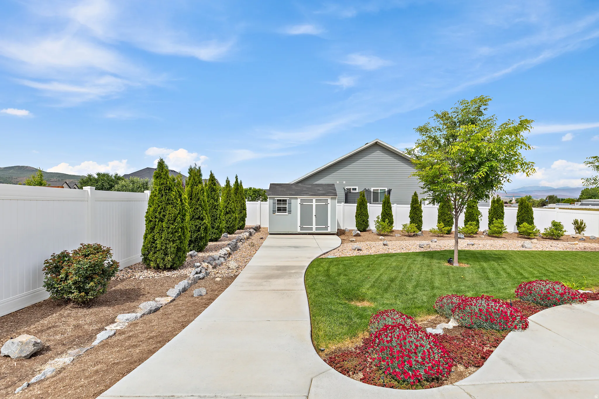 Expansive backyard featuring a lush lawn, mature landscaping, and a white privacy fence