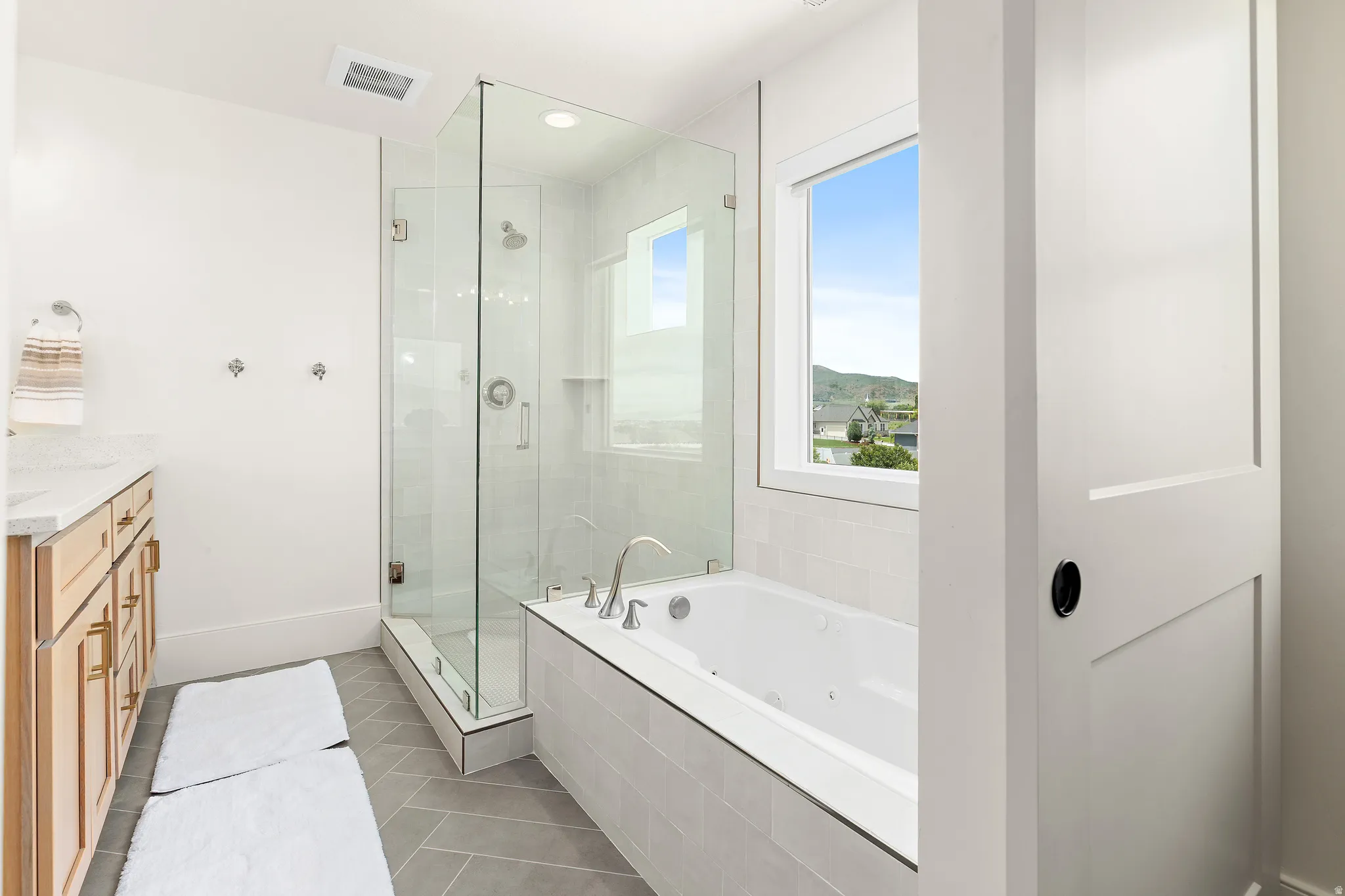 Bathroom featuring a glass-enclosed shower, a built-in soaking tub, and a wood-finish vanity with a light-toned countertop