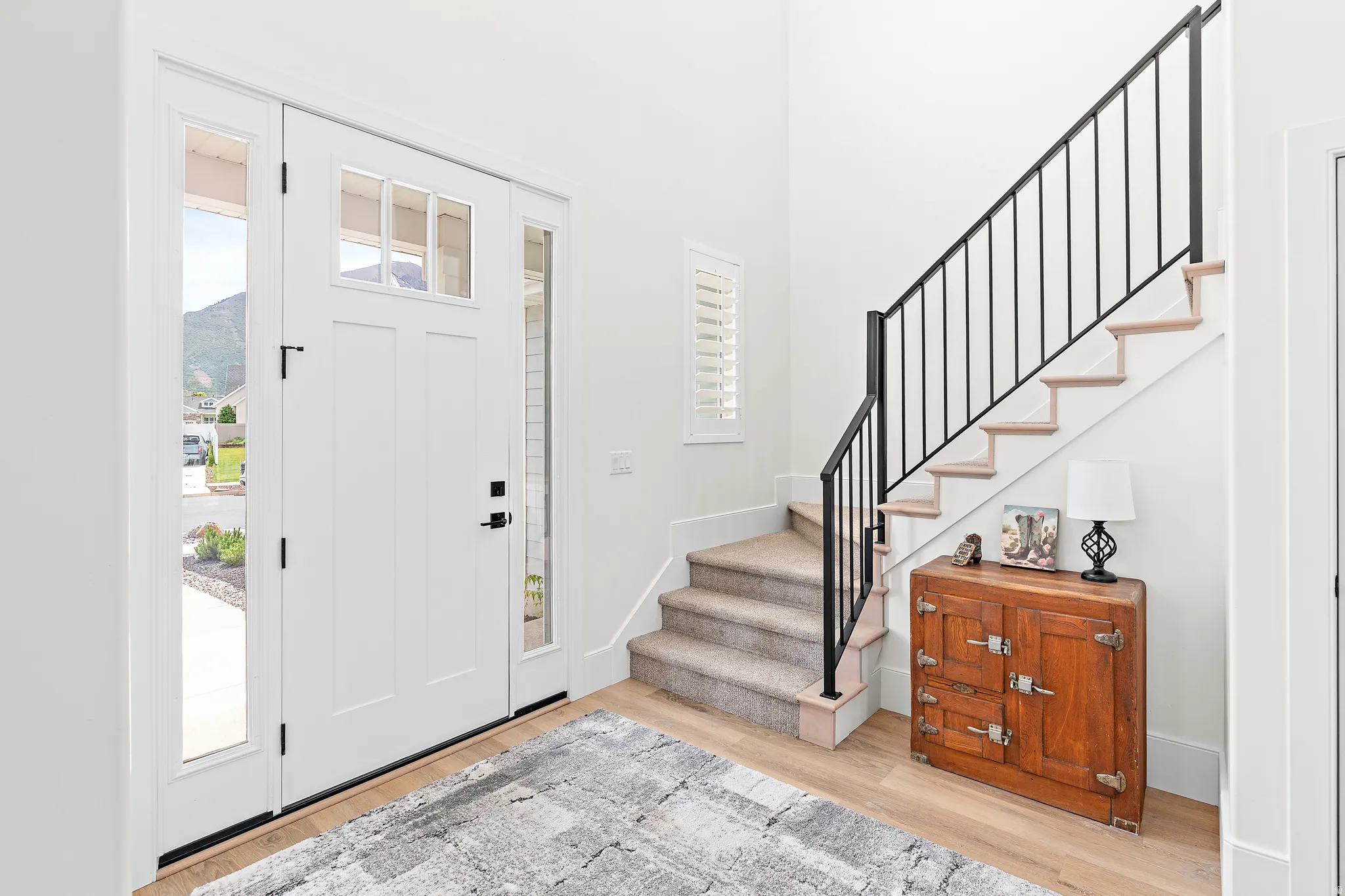 Entryway featuring wood-finish flooring, a white paneled door with transom and sidelight windows, and a staircase with a black metal railing