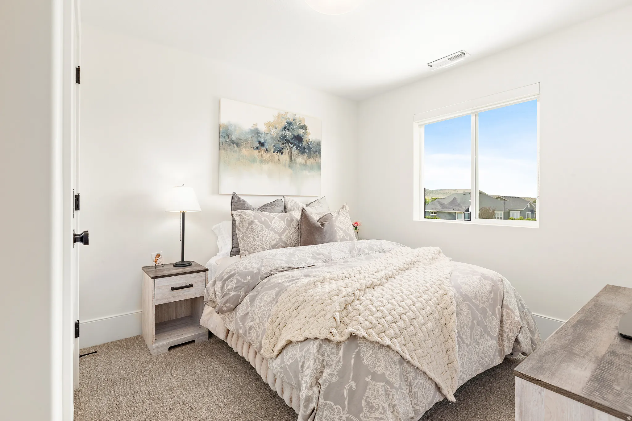 Bright bedroom featuring a large window, plush carpet, and a neutral color palette