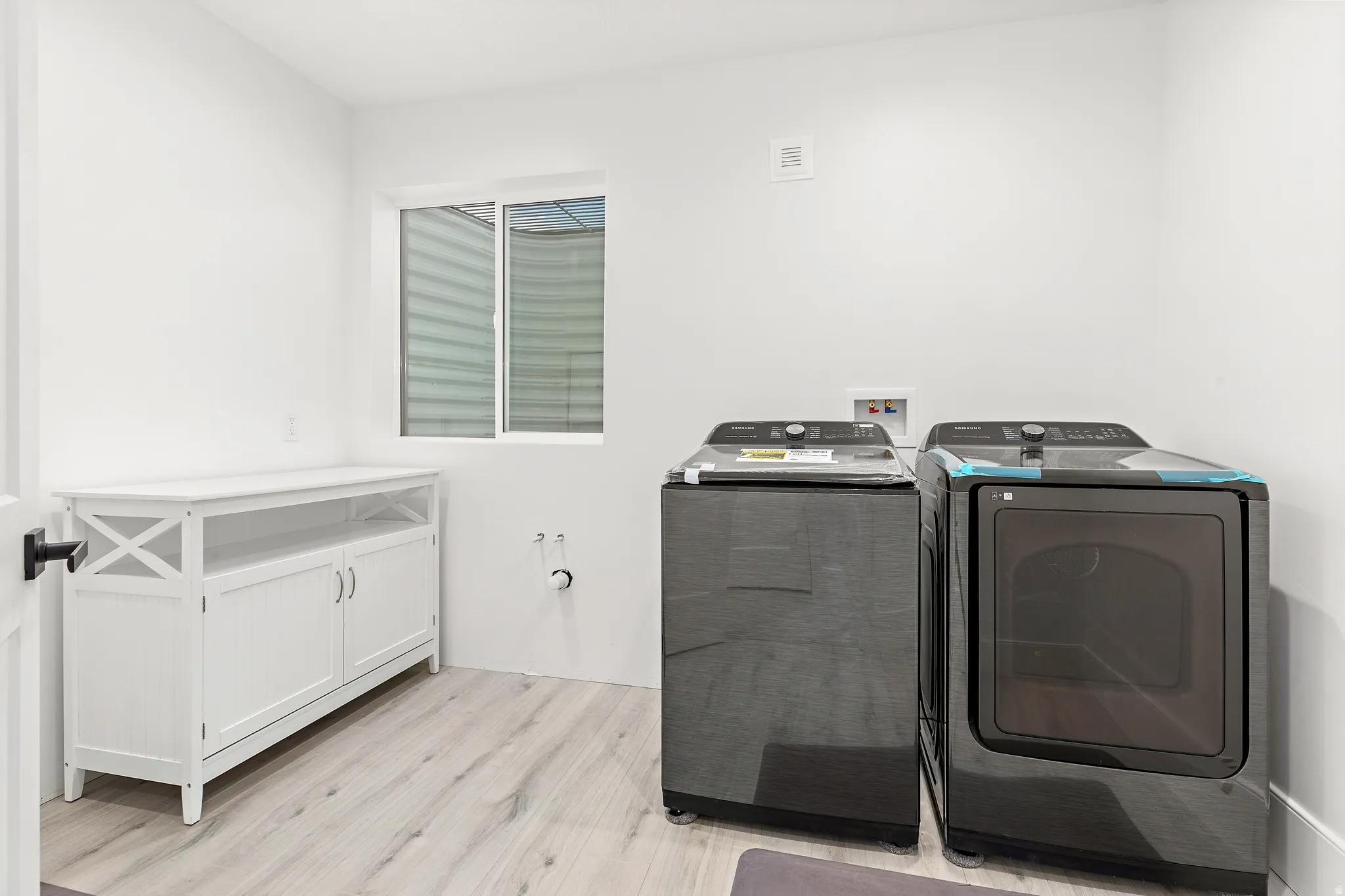 Laundry room featuring light wood-finish flooring, a white built-in storage cabinet, a window, and white walls