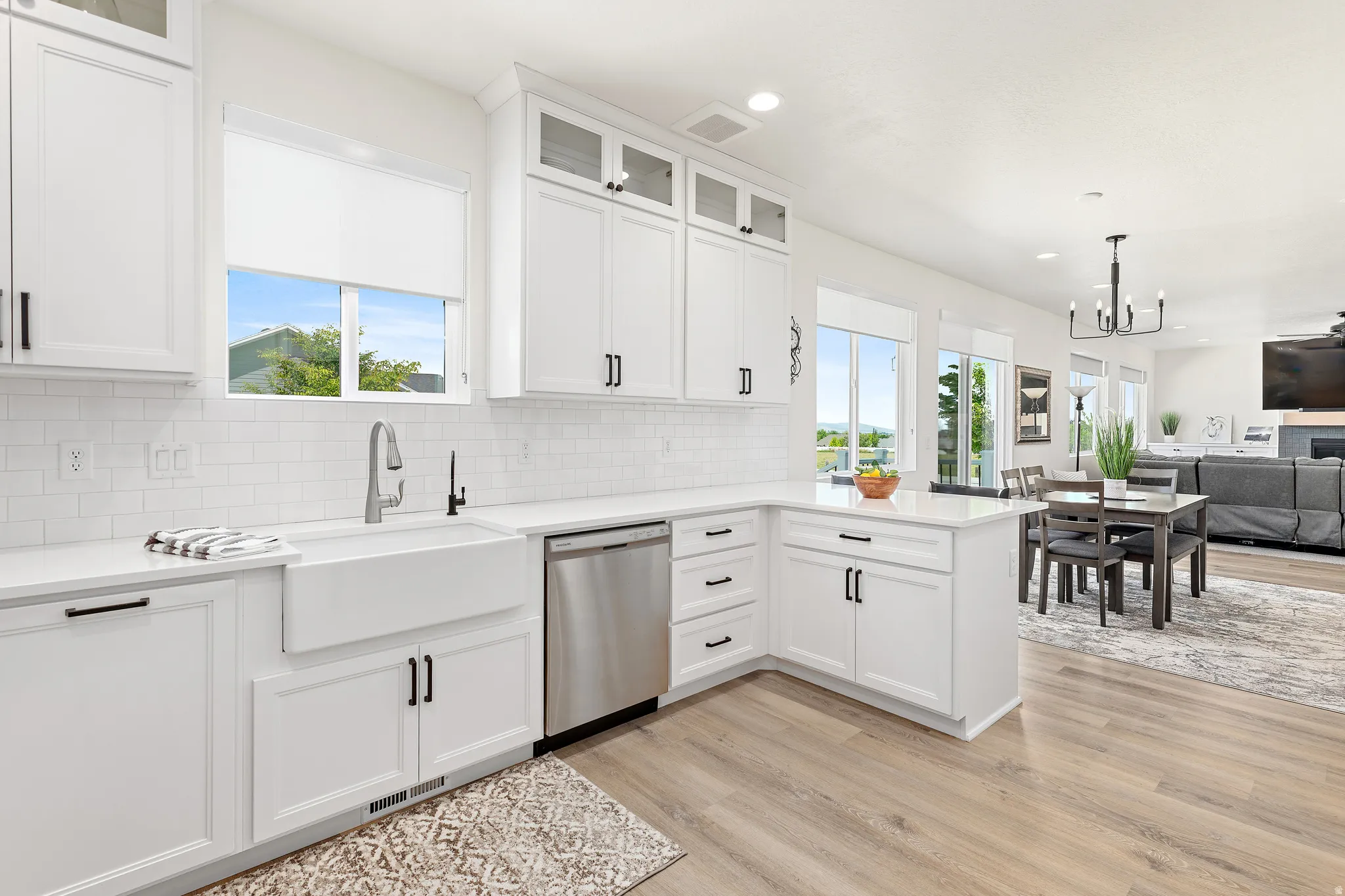 Bright kitchen featuring white shaker cabinetry, an apron front sink, stainless steel dishwasher, and wood-finish flooring