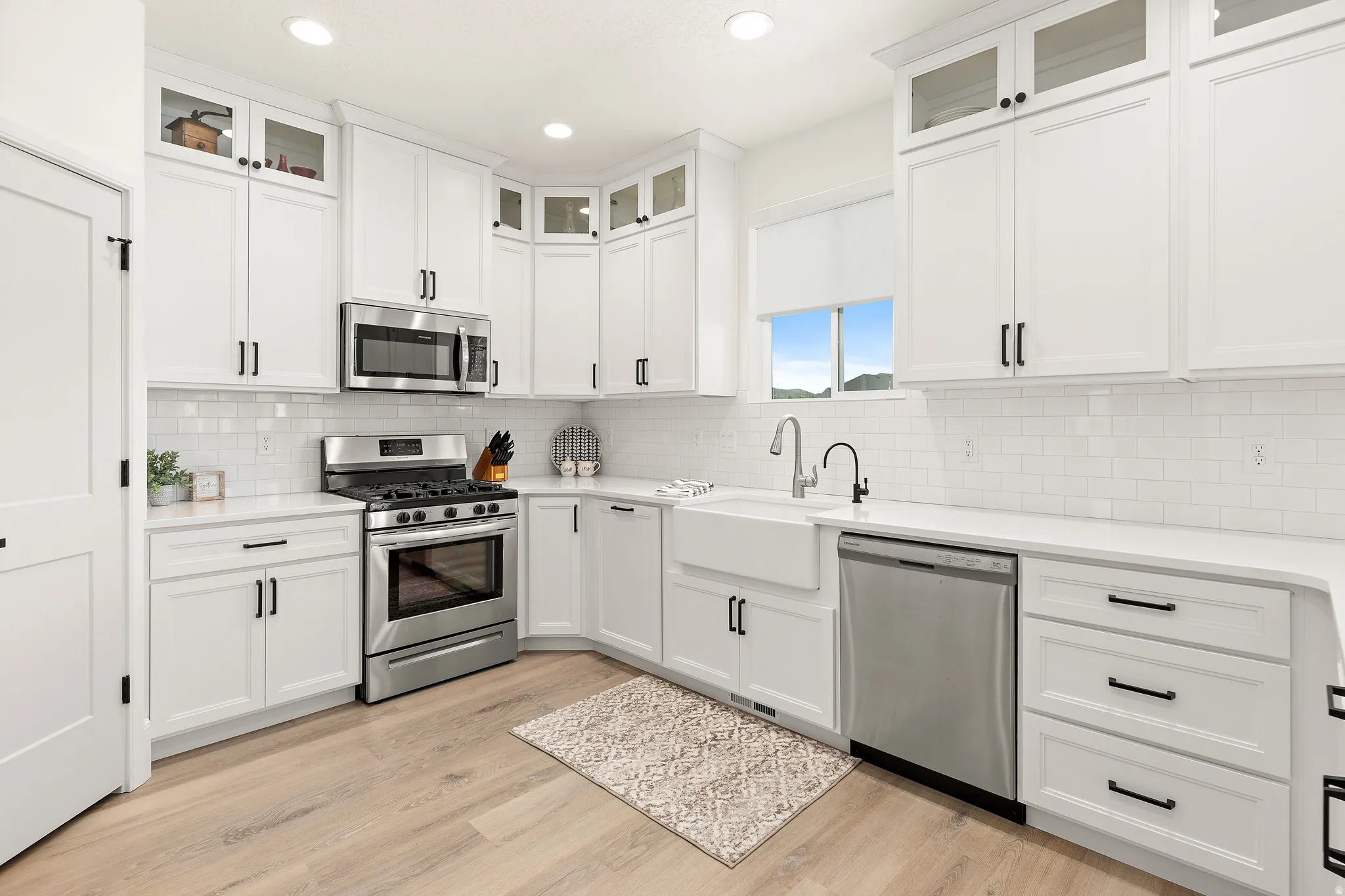 Spacious kitchen featuring white cabinetry, light countertops, wood-finish flooring, stainless steel appliances, and a farmhouse sink