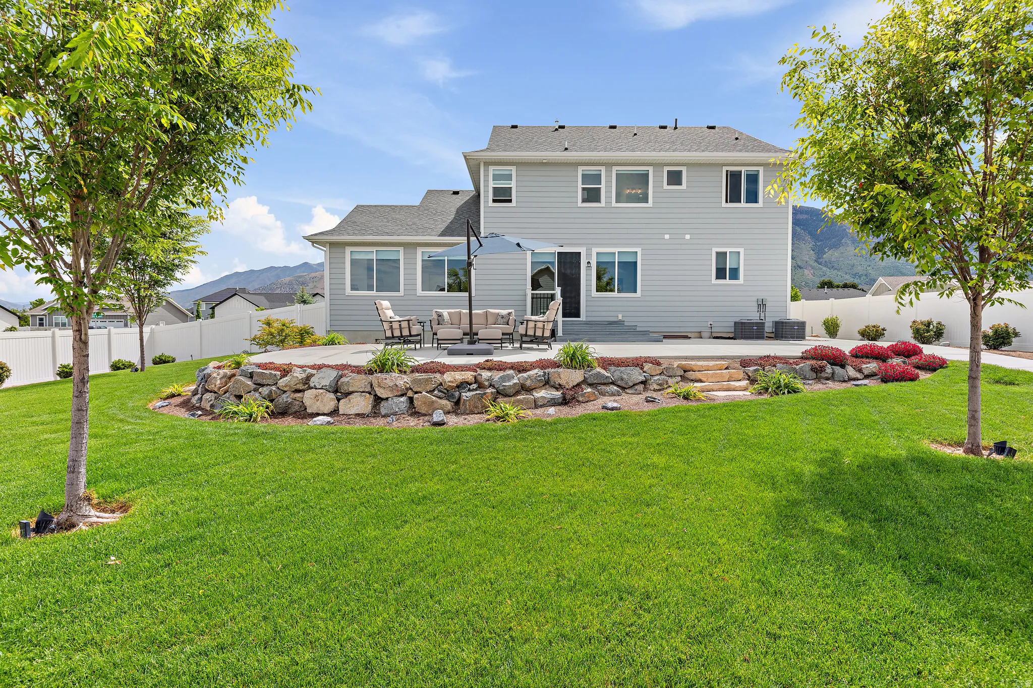 Expansive backyard featuring a manicured lawn, a multi-level patio, and a stone retaining wall