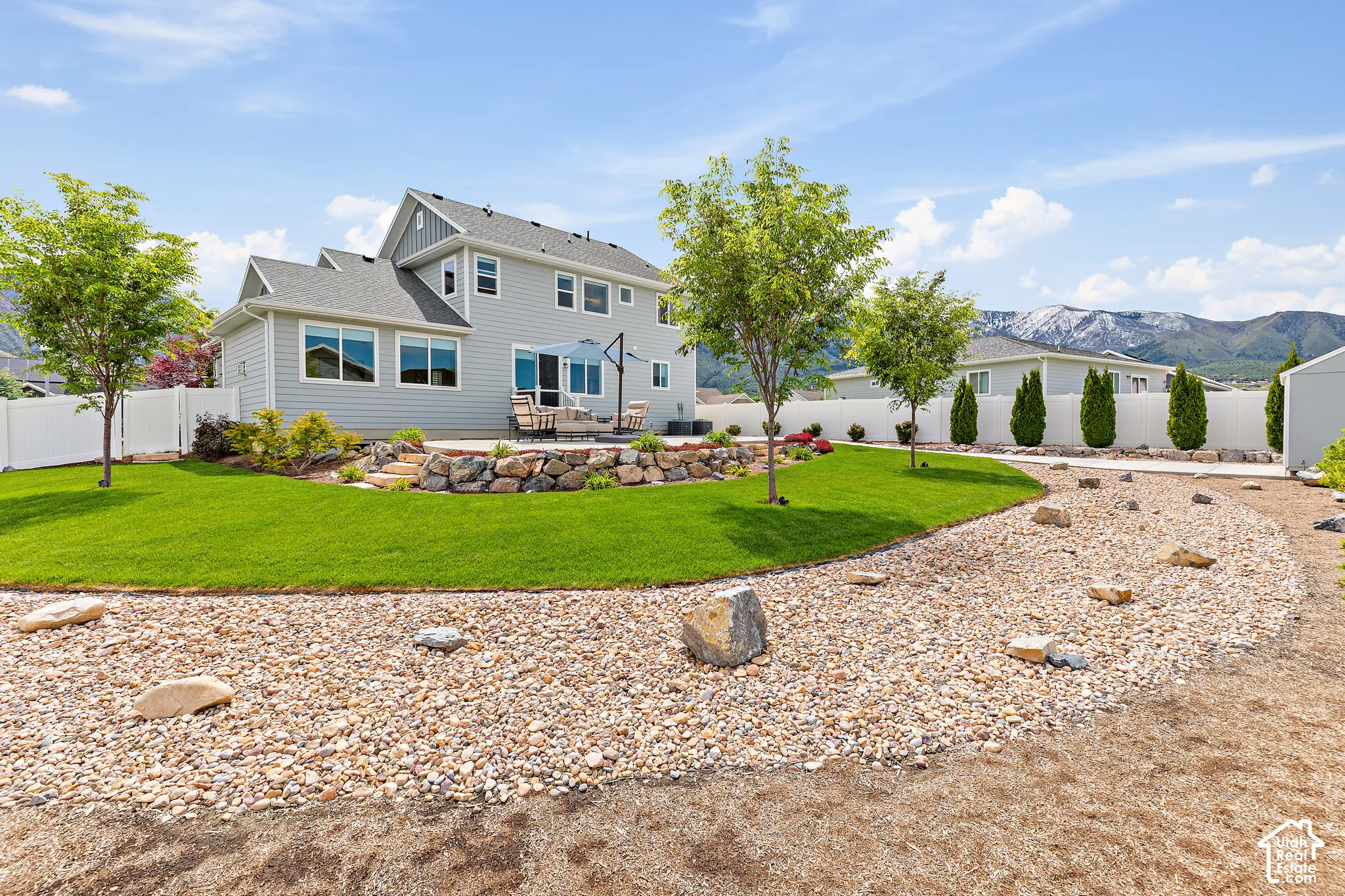 Spacious backyard featuring a manicured lawn, a gravel bed with scattered rocks, and mature trees