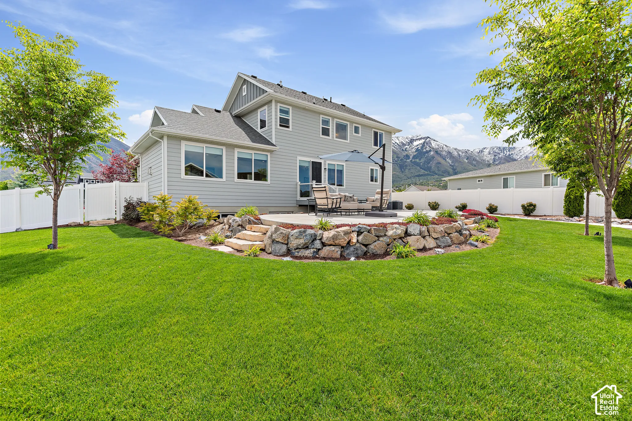 Spacious backyard featuring a large green lawn, a stone-tiered patio, and a retaining wall with integrated landscaping