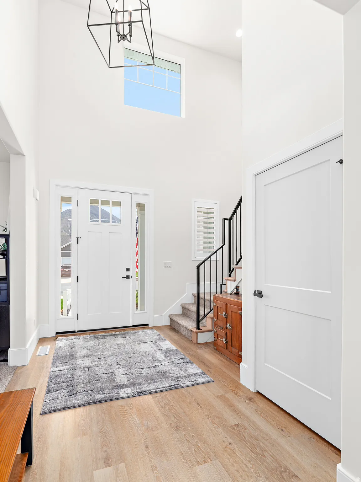 Two-story foyer featuring light wood-finish flooring, a contemporary chandelier, and a prominent transom window