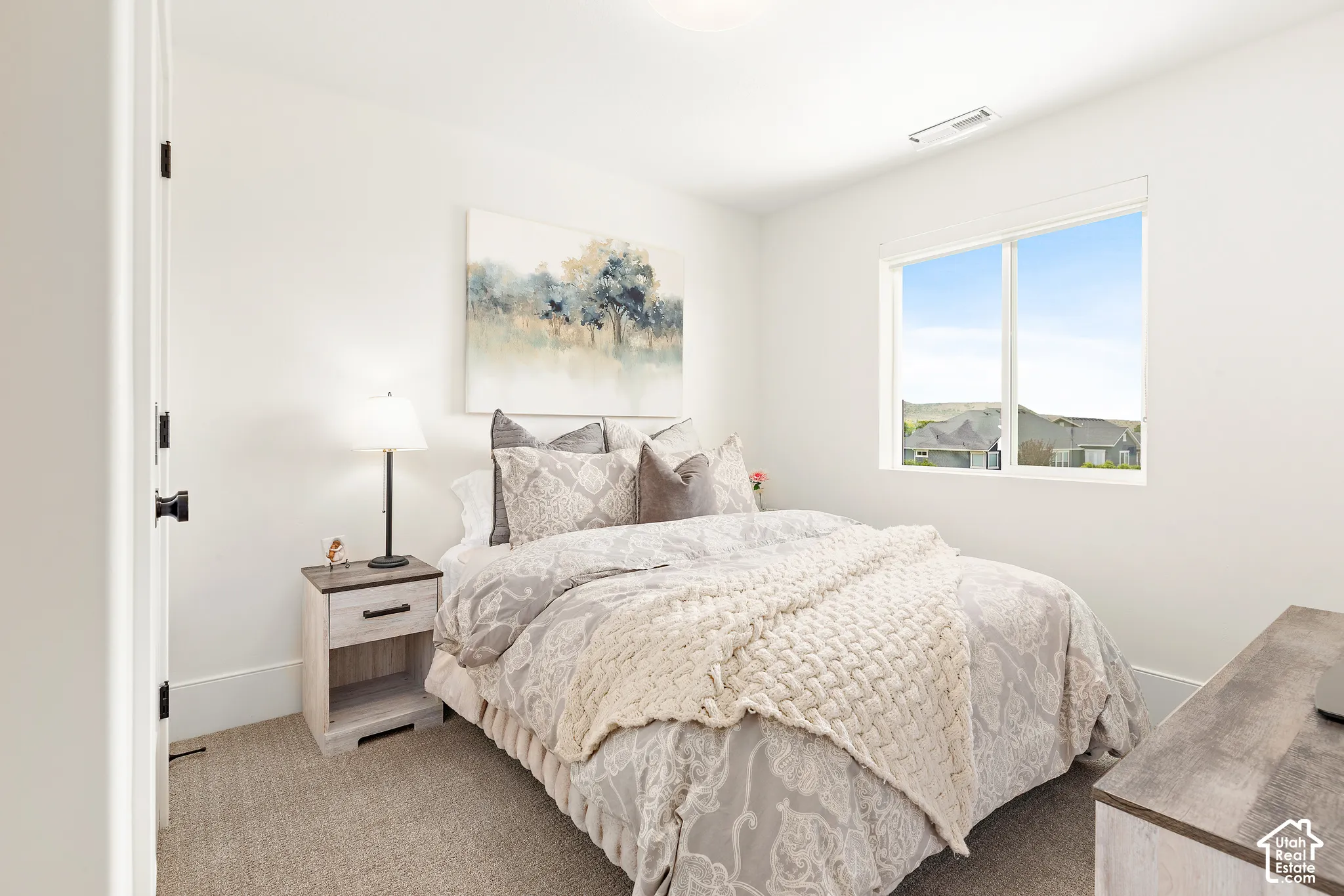 Bright bedroom featuring a large window, plush carpet, and a neutral color palette