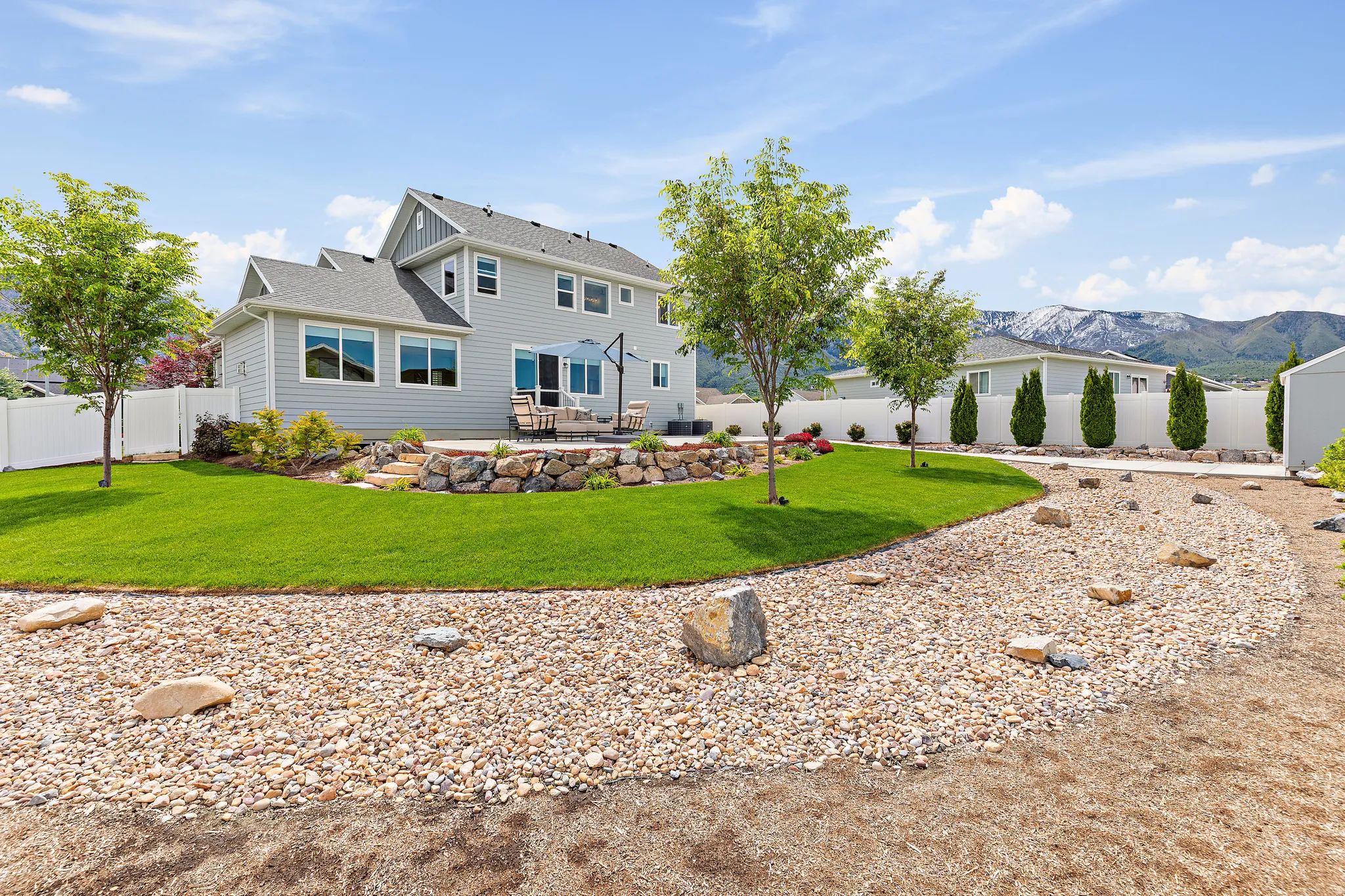 Spacious backyard featuring a manicured lawn, a gravel bed with scattered rocks, and mature trees