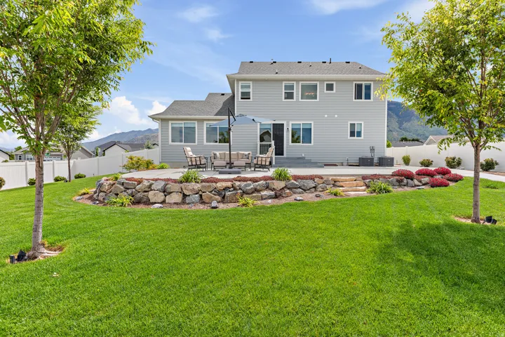 Expansive backyard featuring a manicured lawn, a multi-level patio, and a stone retaining wall