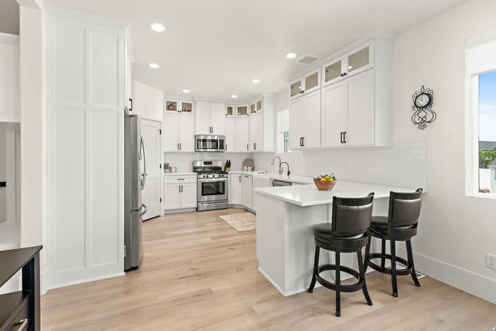 Bright kitchen featuring white cabinetry, stainless steel appliances, a white subway tile backsplash, light wood-finish flooring, and a peninsula with countertop seating