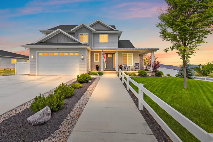 Two-story residence featuring a covered front porch, an attached two-car garage, and a white picket fence bordering a manicured lawn