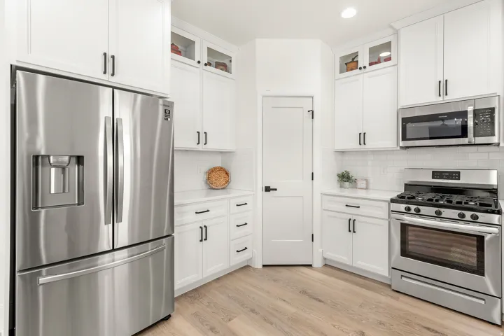 Kitchen featuring white cabinetry with dark hardware, stainless steel appliances including a French door refrigerator and gas range, white subway tile backsplash, light wood-finish flooring, and white countertops