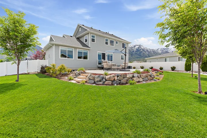 Spacious backyard featuring a large green lawn, a stone-tiered patio, and a retaining wall with integrated landscaping