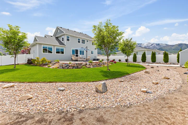 Spacious backyard featuring a manicured lawn, a gravel bed with scattered rocks, and mature trees