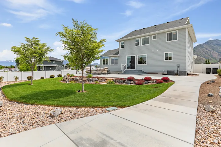 Expansive backyard featuring a manicured lawn, concrete patio, and mature trees
