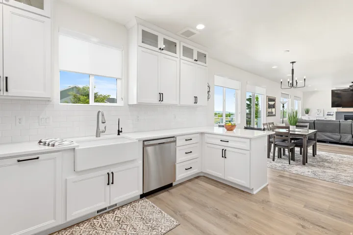 Bright kitchen featuring white shaker cabinetry, an apron front sink, stainless steel dishwasher, and wood-finish flooring