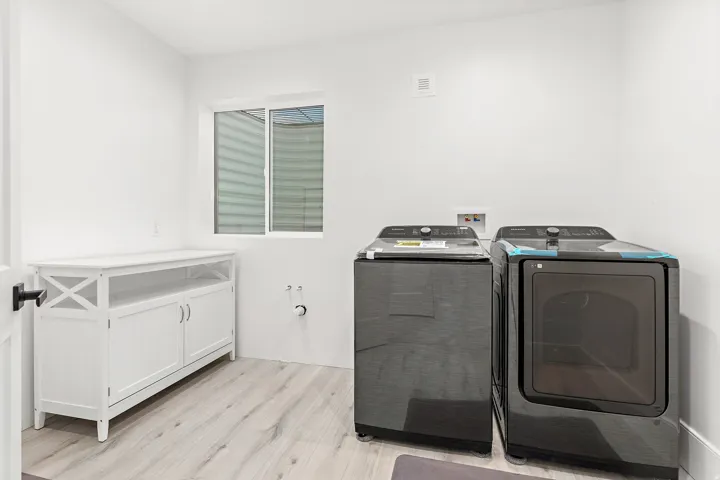 Laundry room featuring light wood-finish flooring, a white built-in storage cabinet, a window, and white walls