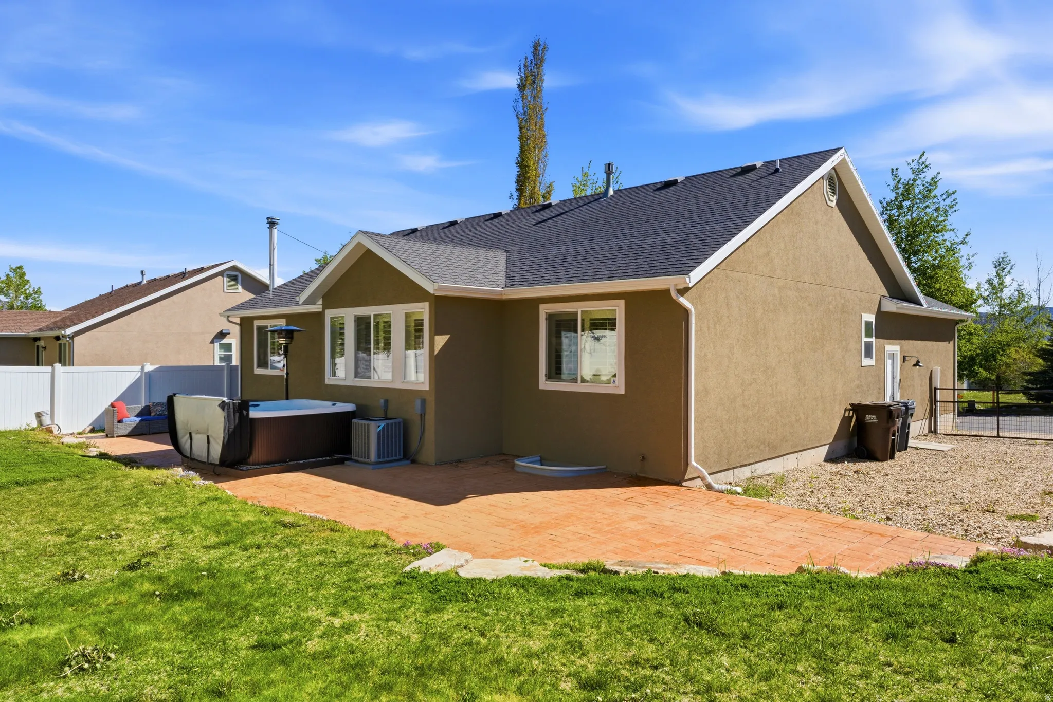 Rear exterior featuring a stamped concrete patio, hot tub, stucco siding, multi-pane windows, and dark asphalt shingle roofing