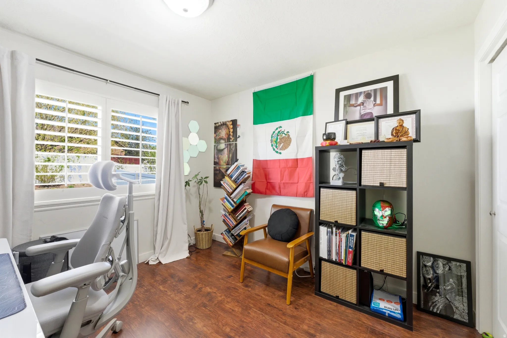 Room featuring wood-finish flooring, white walls, and a window with plantation shutters and white curtains