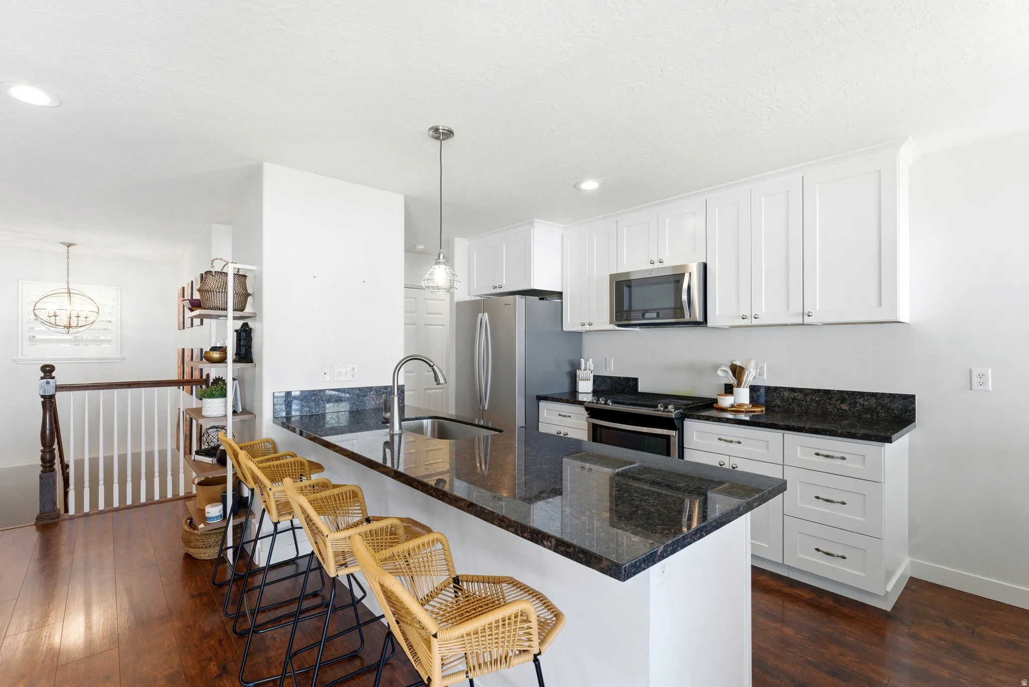 Kitchen featuring an island with a sink, white cabinetry, stainless steel appliances, dark countertops, and wood-finish flooring