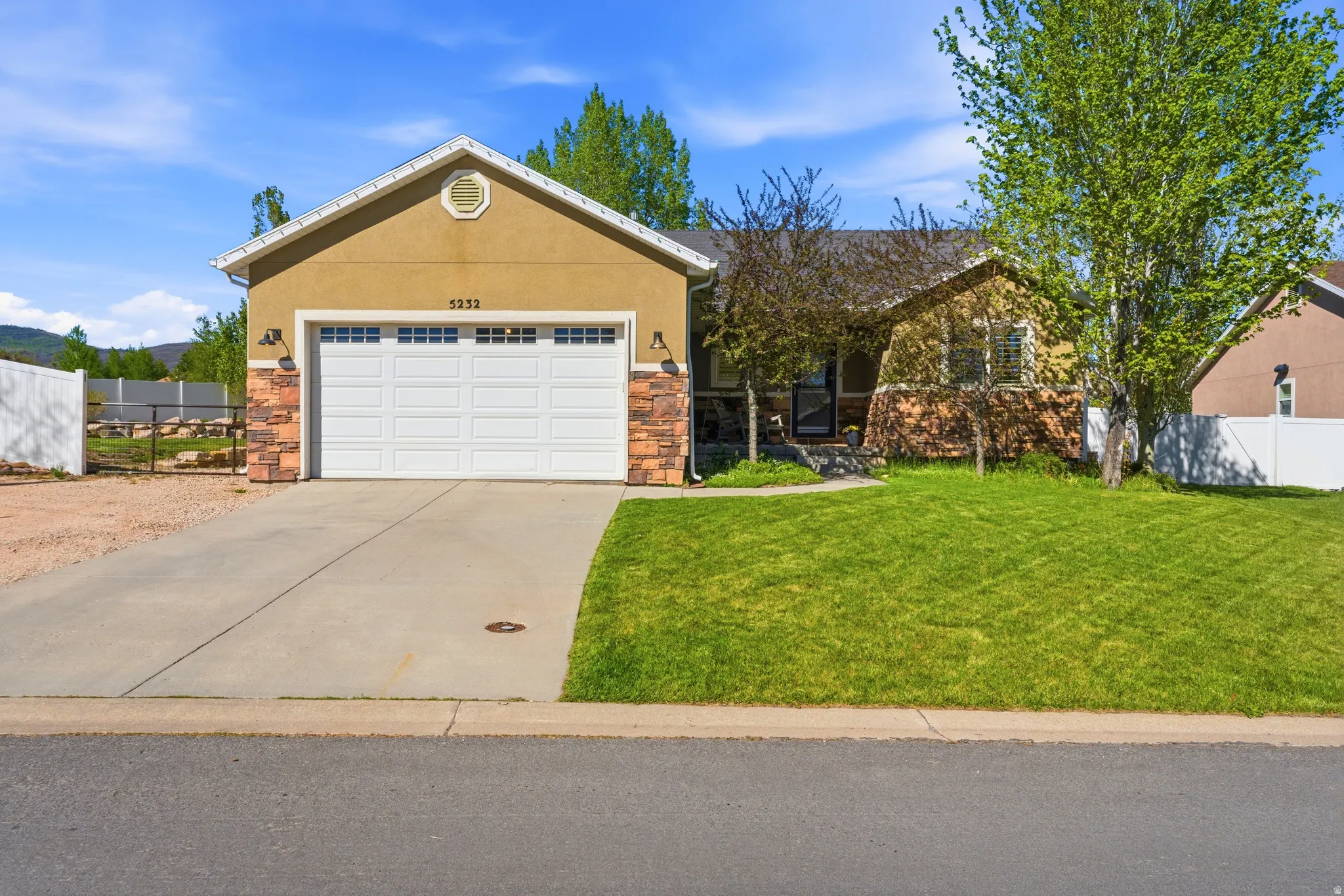 Single-story residence featuring a two-car garage with a white sectional door, a stucco and stone veneer exterior, a concrete driveway, and a front lawn with mature trees