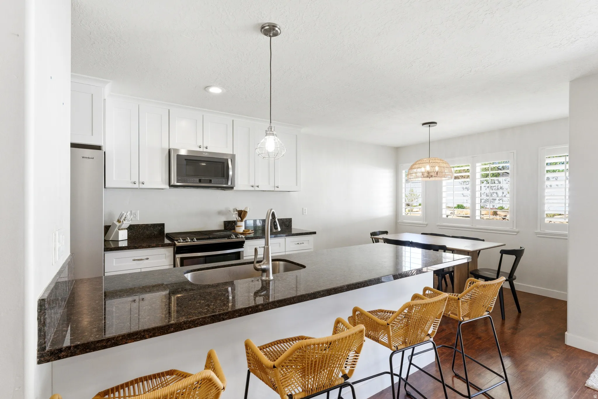 Kitchen featuring white cabinetry, dark granite-style countertops, stainless steel appliances, and a large breakfast bar with sink