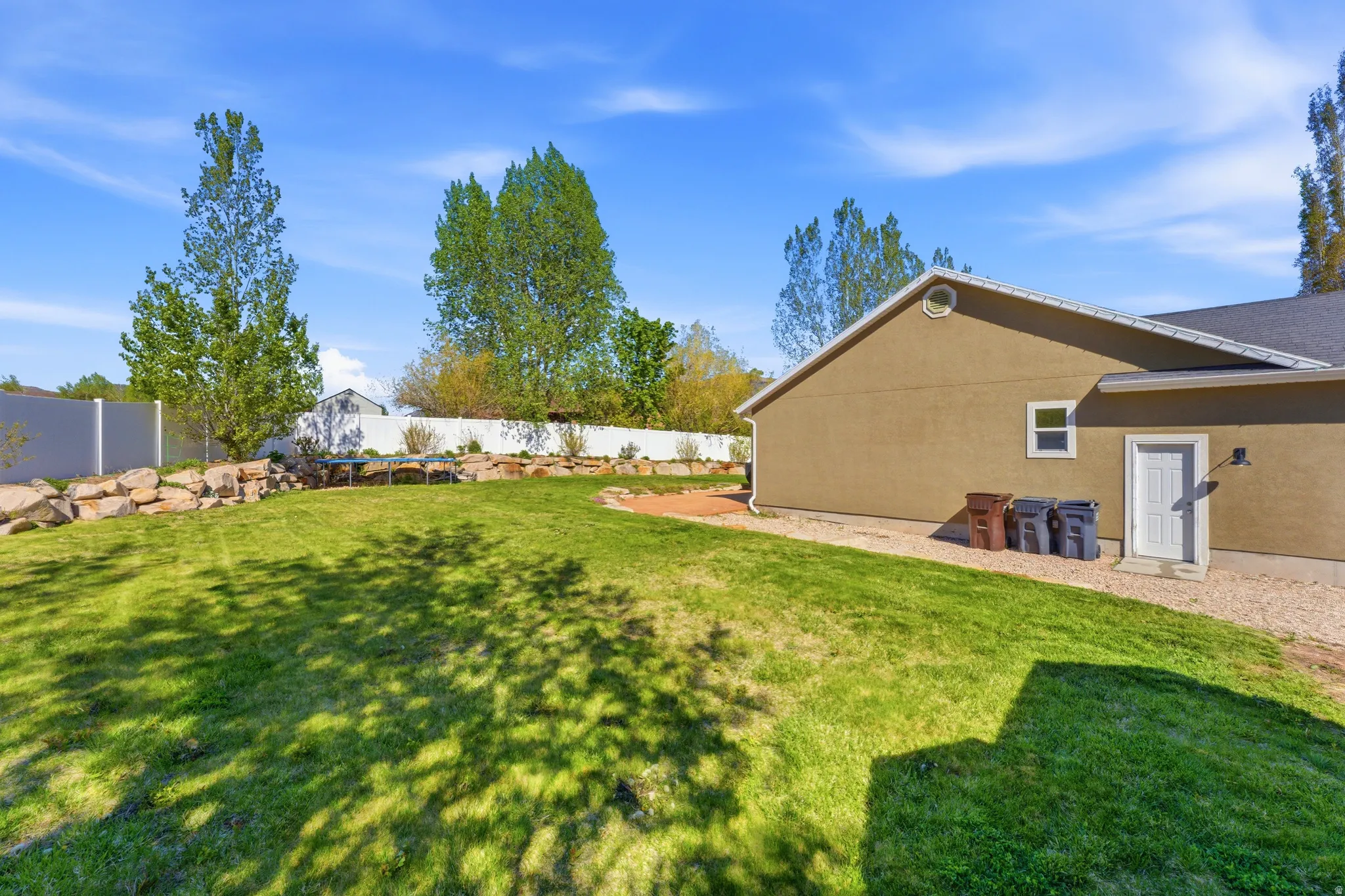 Expansive green lawn with a tiered rock retaining wall and a white vinyl privacy fence