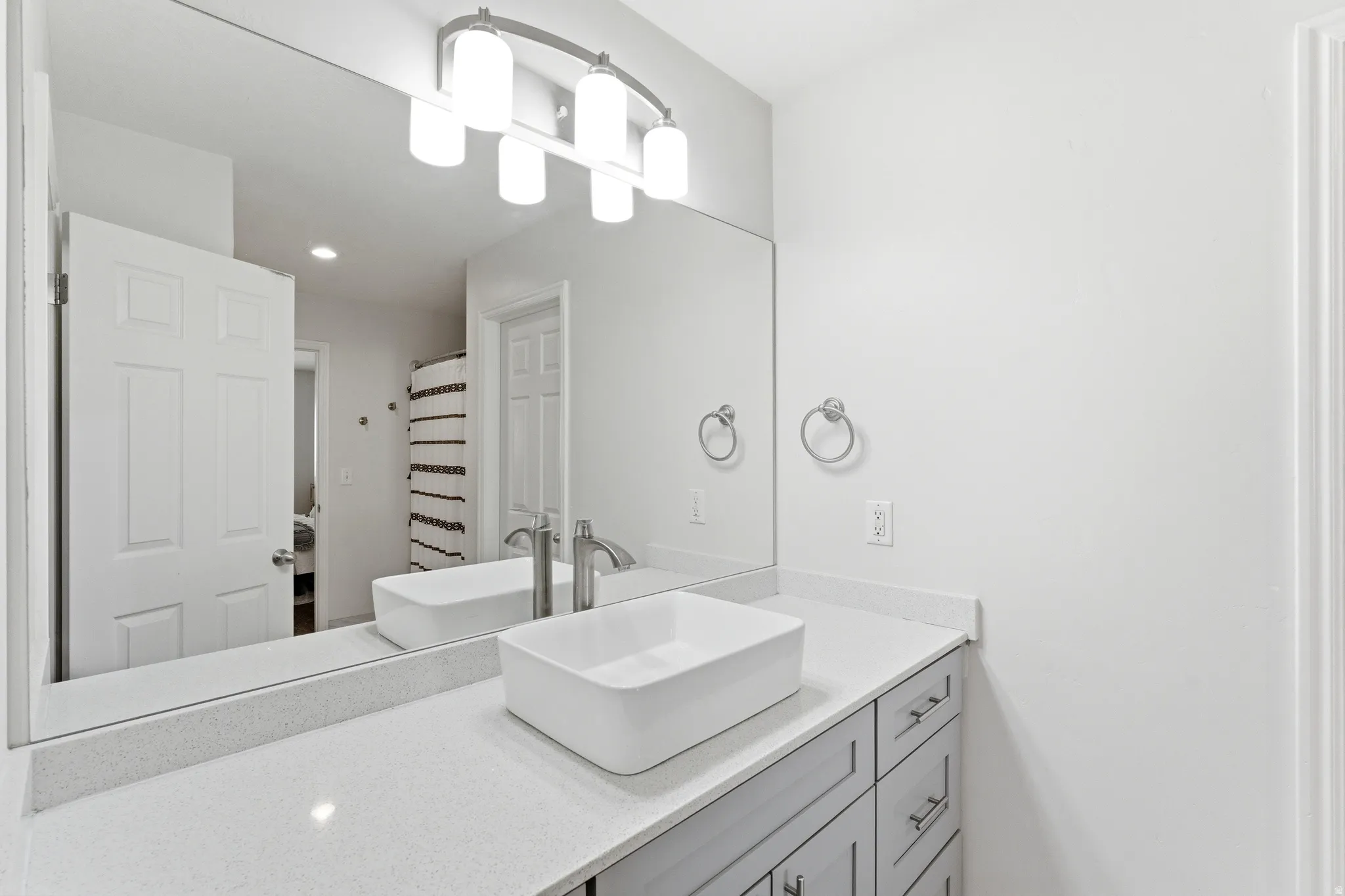 Modern vanity featuring a vessel sink, a light-toned countertop, and light gray cabinetry with brushed nickel hardware