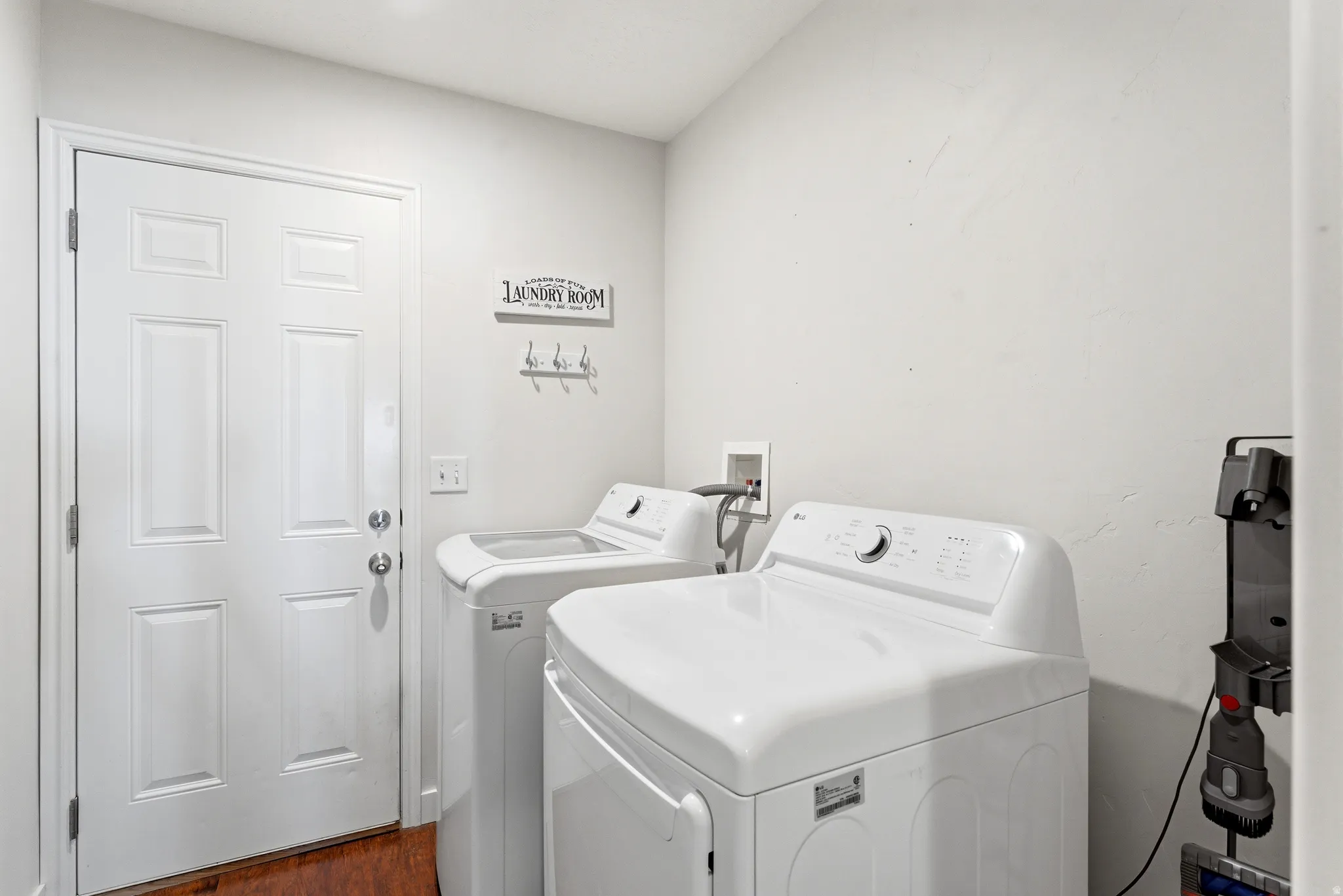 Dedicated laundry area featuring a paneled white door, wood-finish flooring, and a wall-mounted utility hook rack