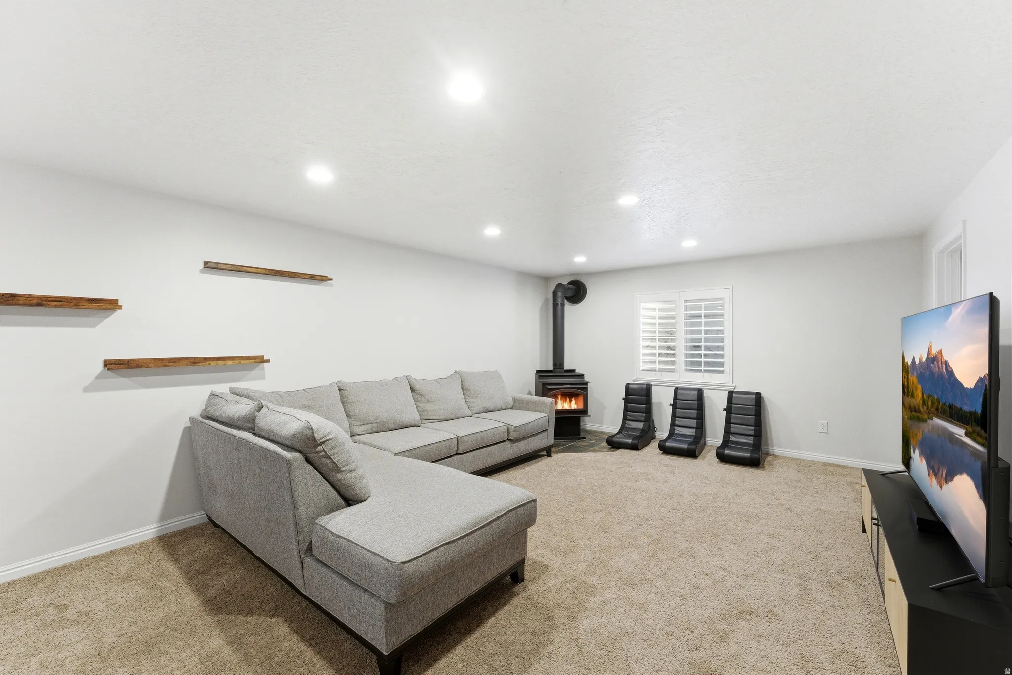 Spacious living area featuring neutral carpeting, recessed lighting, and a modern wood-burning stove with a visible flue