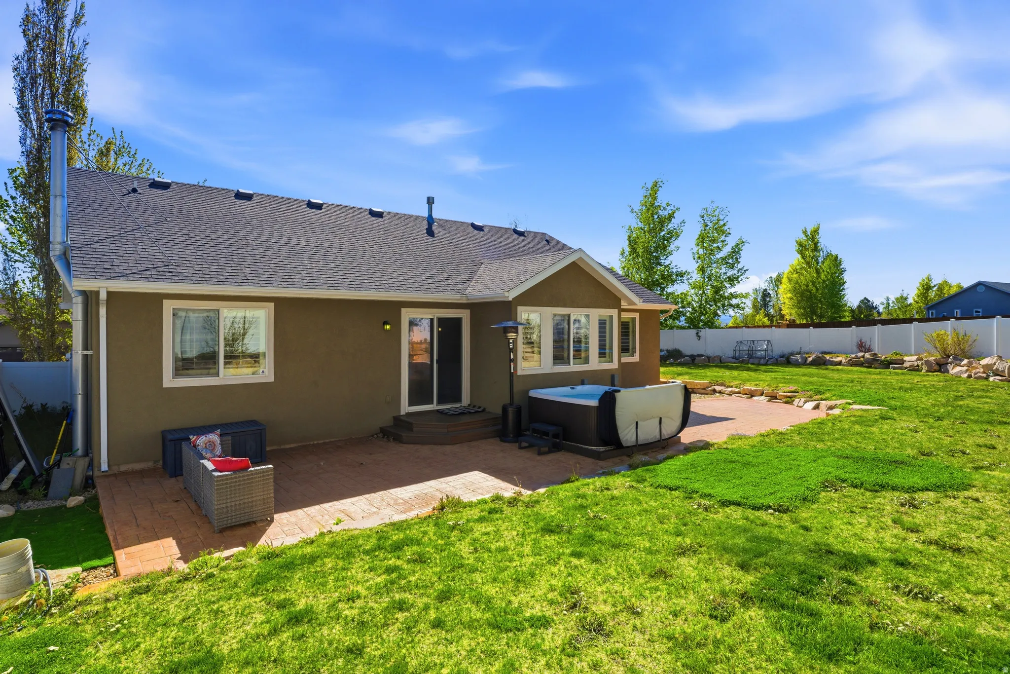 Spacious backyard featuring a large green lawn, a paver patio, and an integrated hot tub