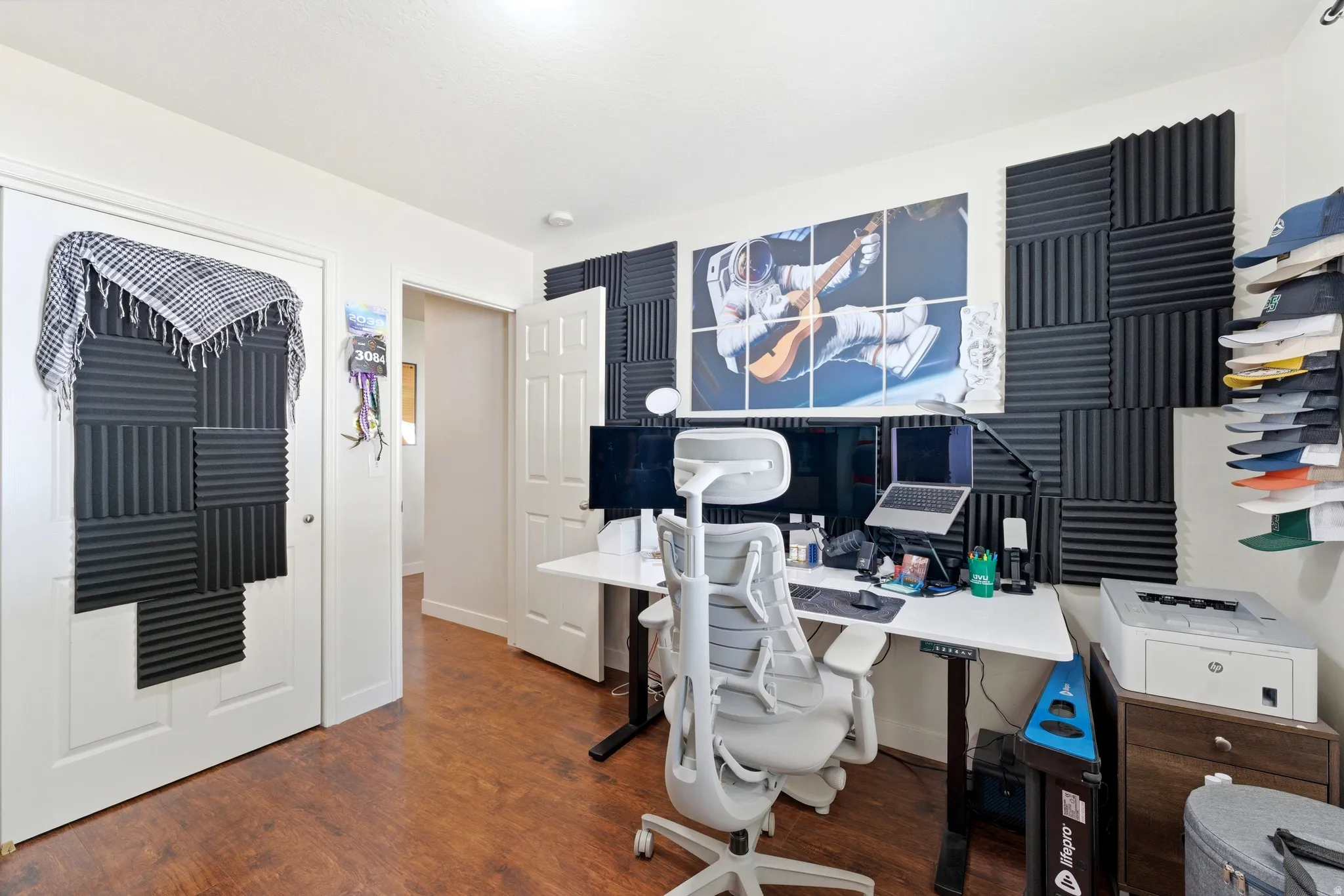 Room featuring wood-finish flooring, white walls, and a built-in wall installation of sound-absorbing panels
