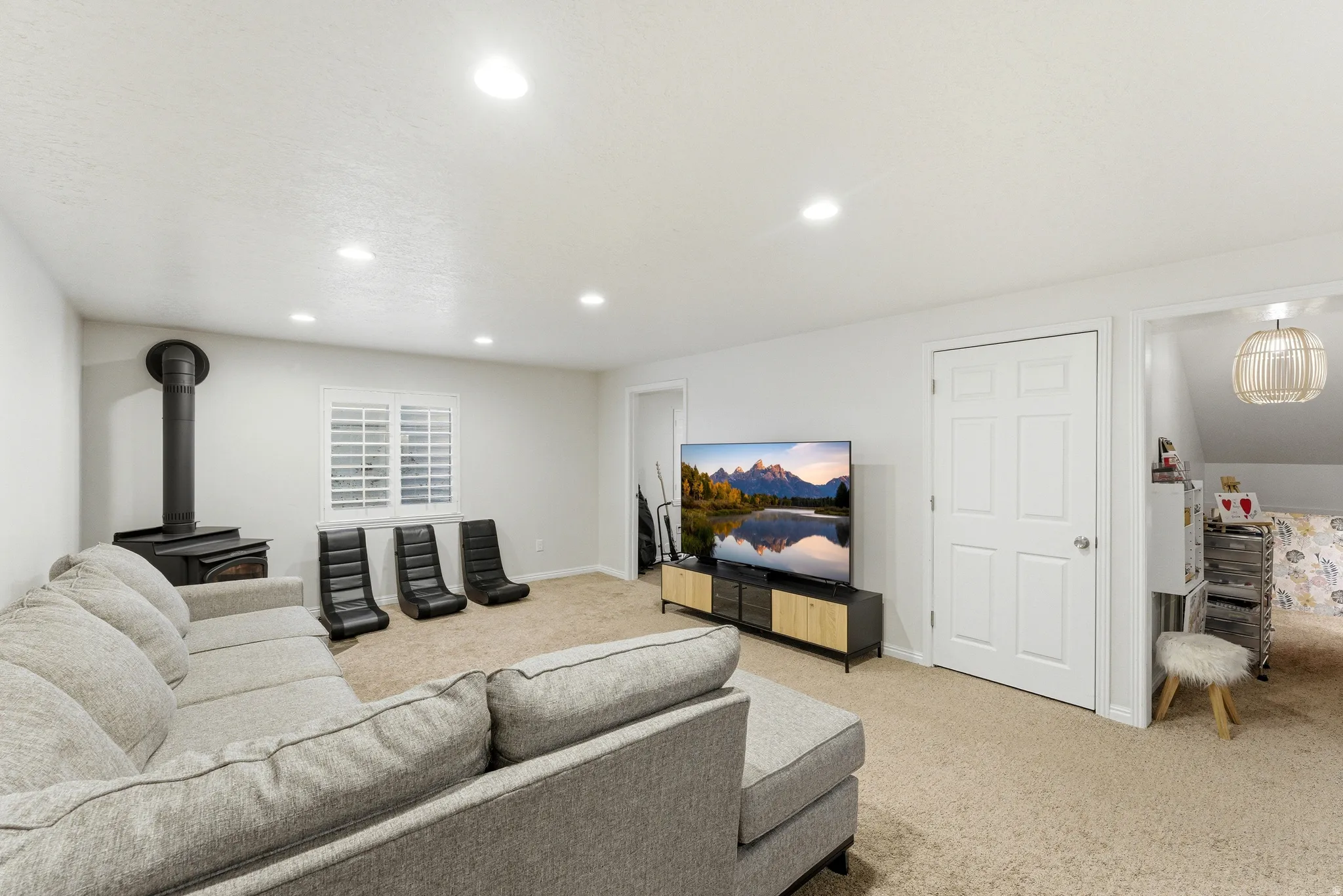 Carpeted living area featuring a black wood stove with pipe, recessed lighting, and a window with plantation shutters